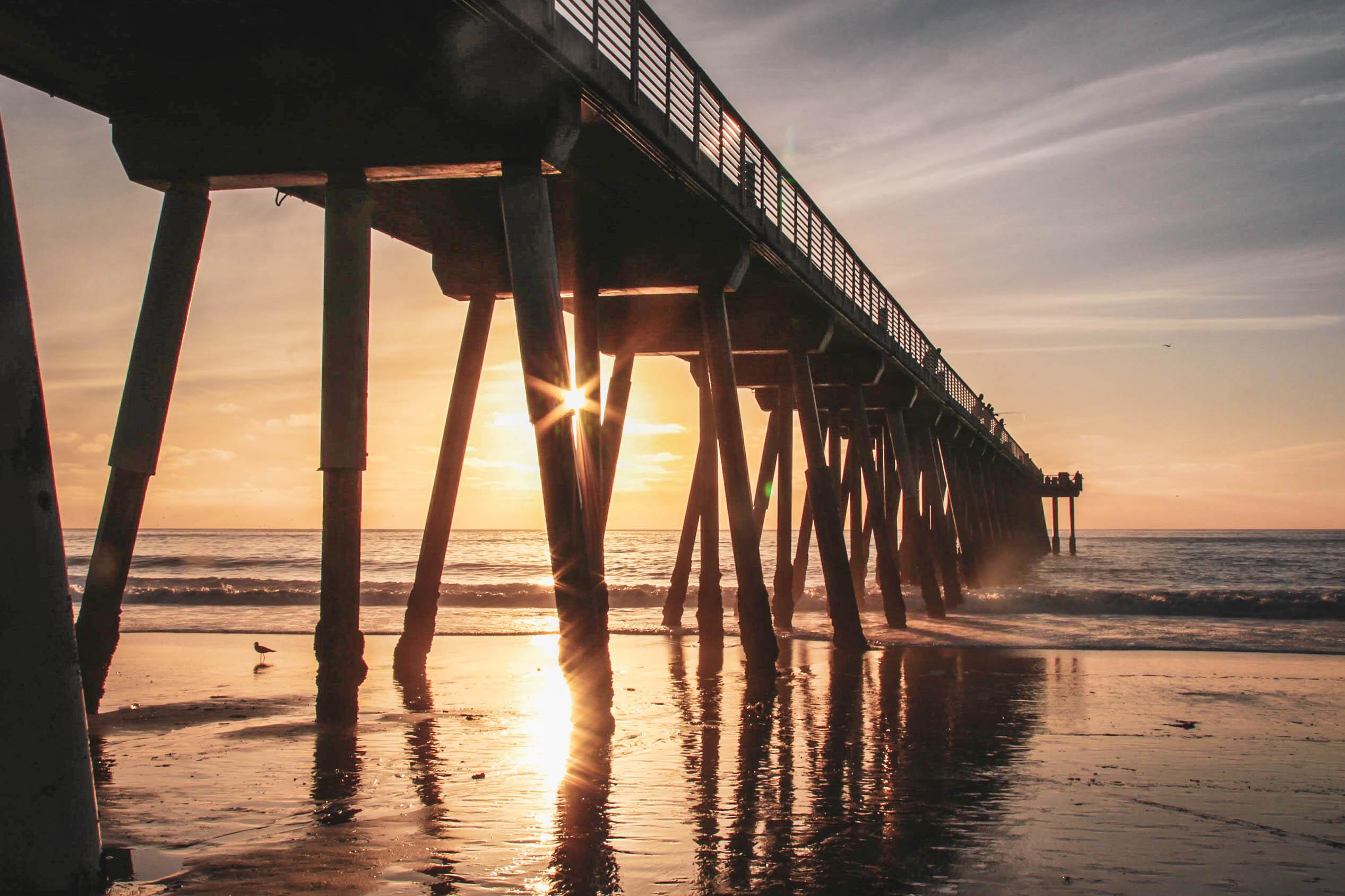 Image of the sunrise shining through the pier over Hermosa Beach in California.