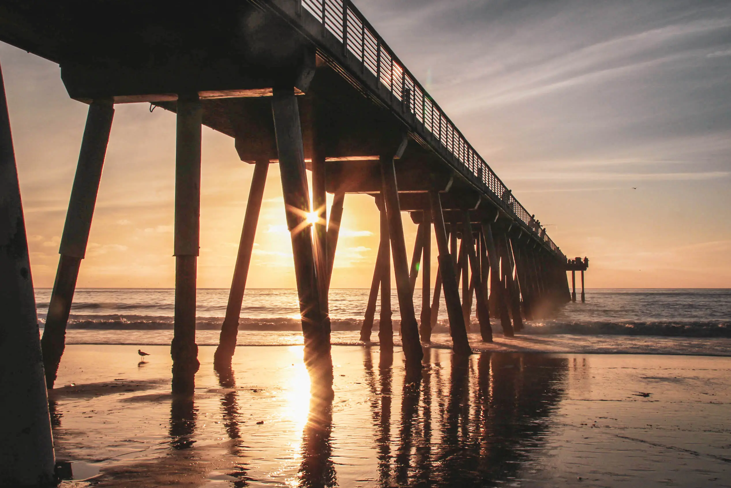 Image of the sunrise shining through the pier over Hermosa Beach in California.