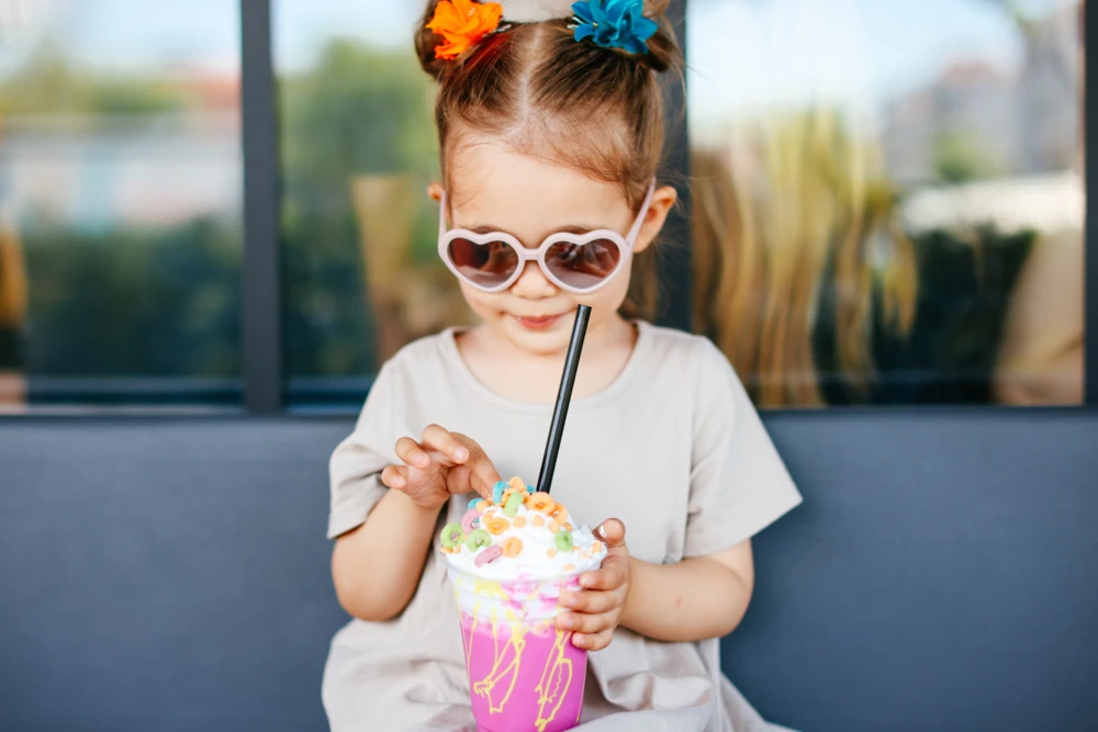 Little girl with sunglasses drinking a fun, whimsical milkshake with a straw