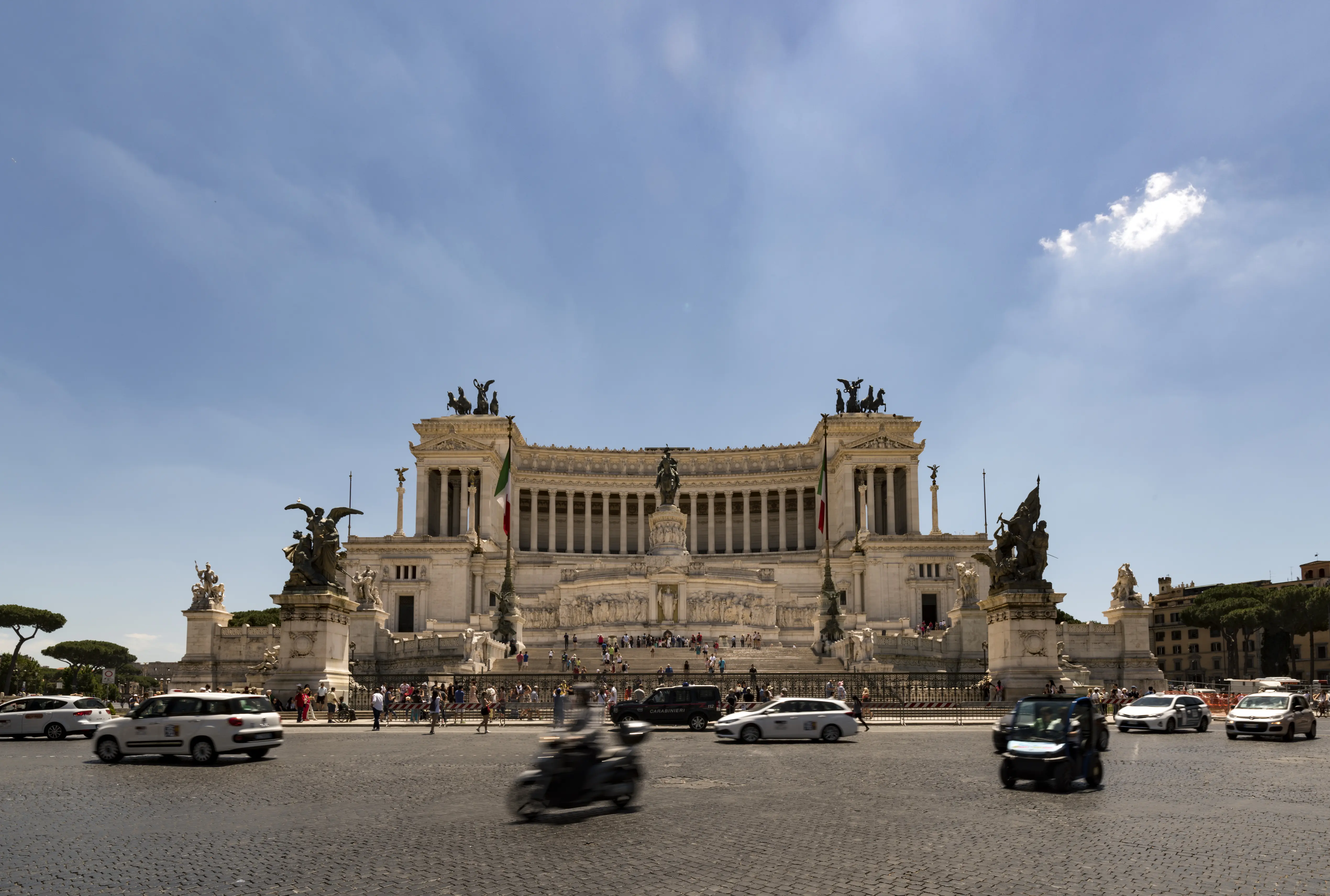 Outdoor daytime image of cars driving in front of Altare della Patria in Rome.
