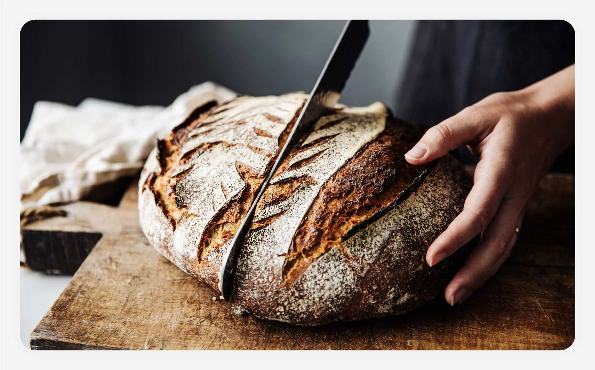 A baker slicing a fresh sourdough loaf on a cutting board.