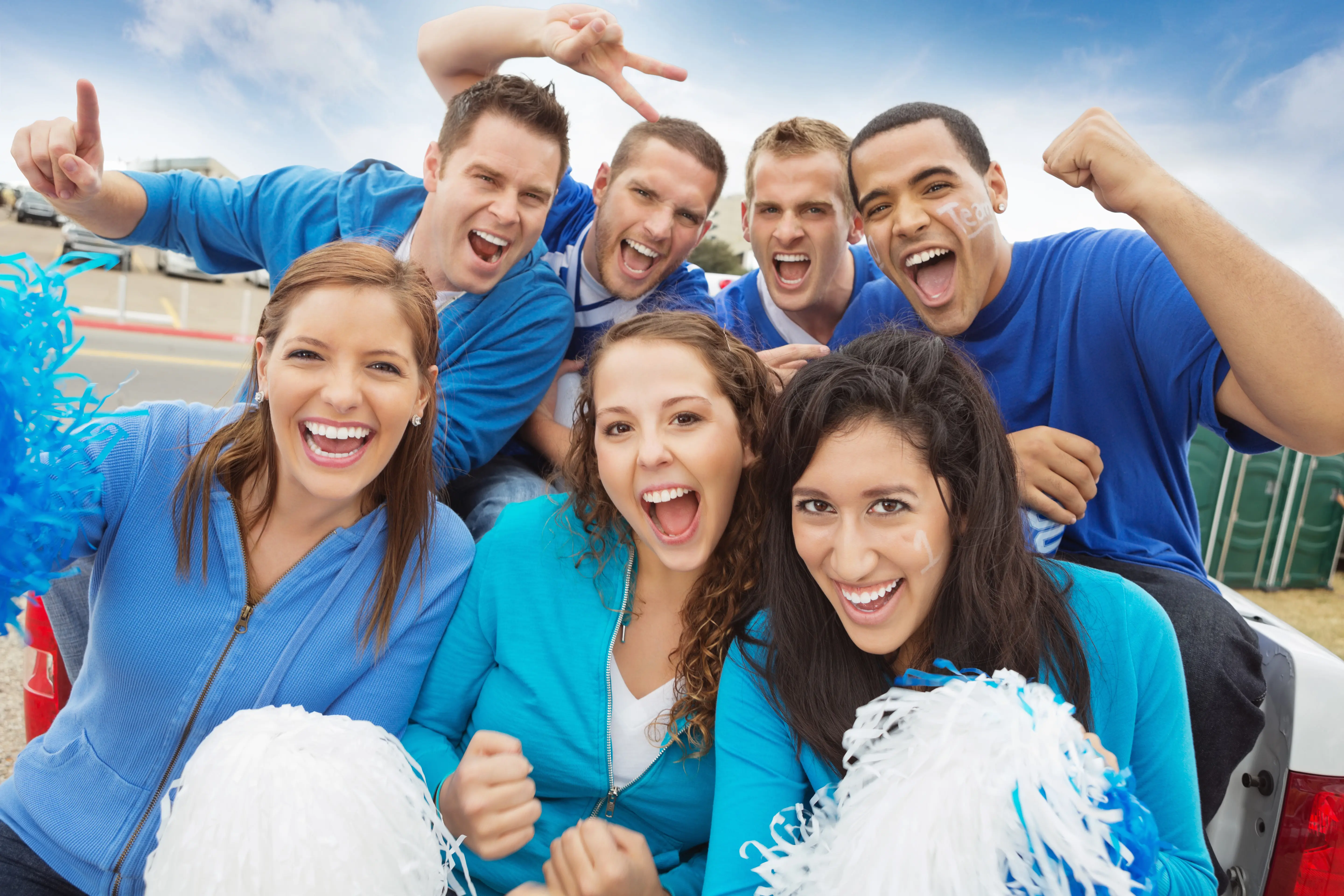 Group of cheering sports fans tailgating at a stadium wearing blue