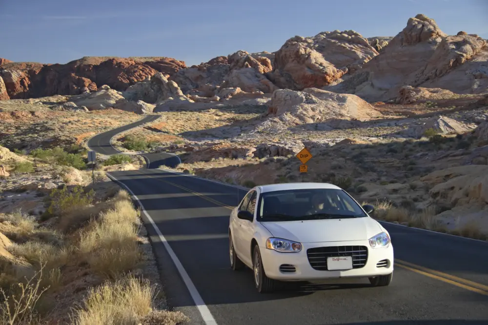 White car driving on a curvy road past rock formations.