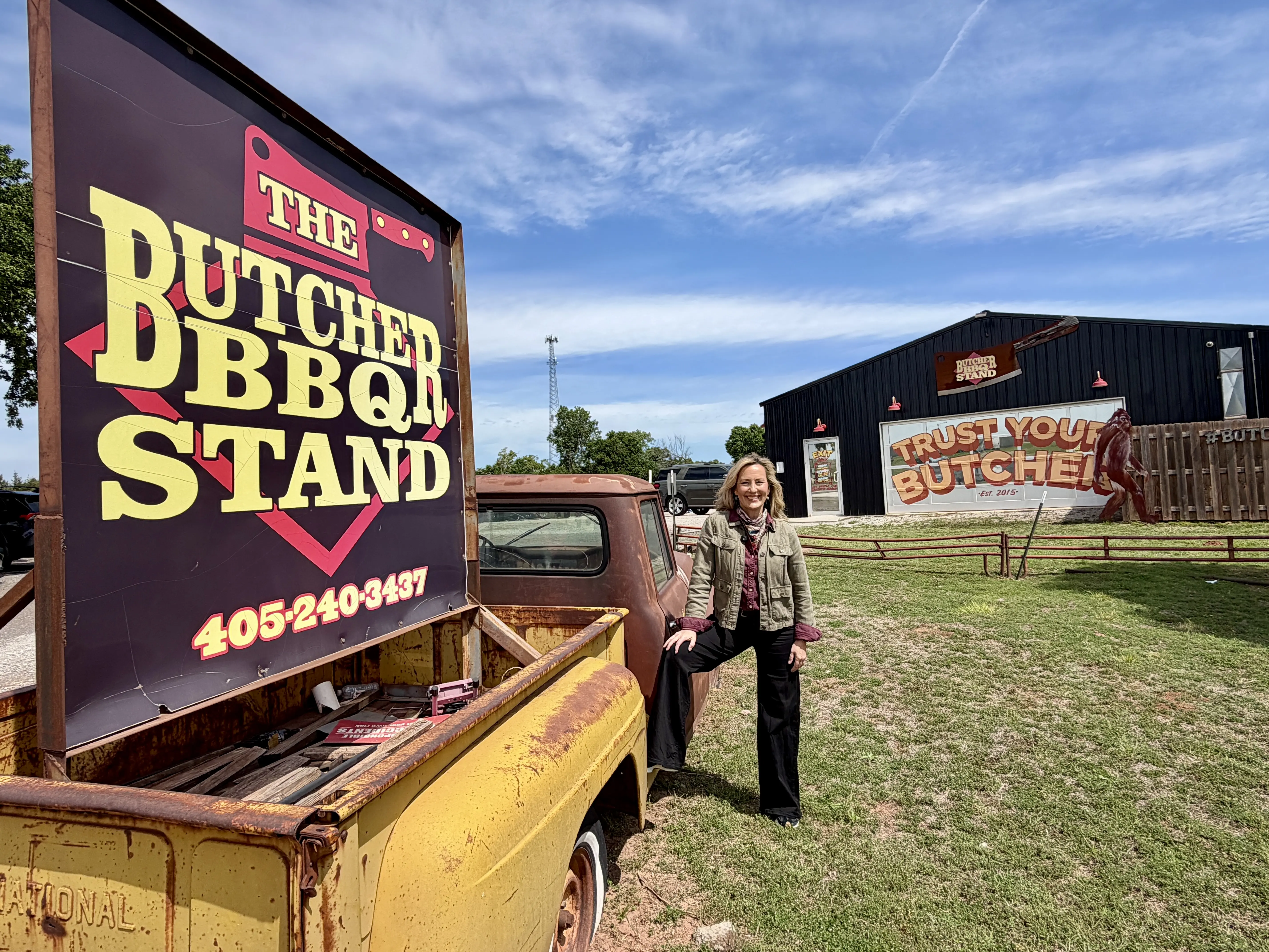 Jennifer Broome stands next to yellow vintage truck with sign for Butcher BBQ Stand mounted in the truck's bed.