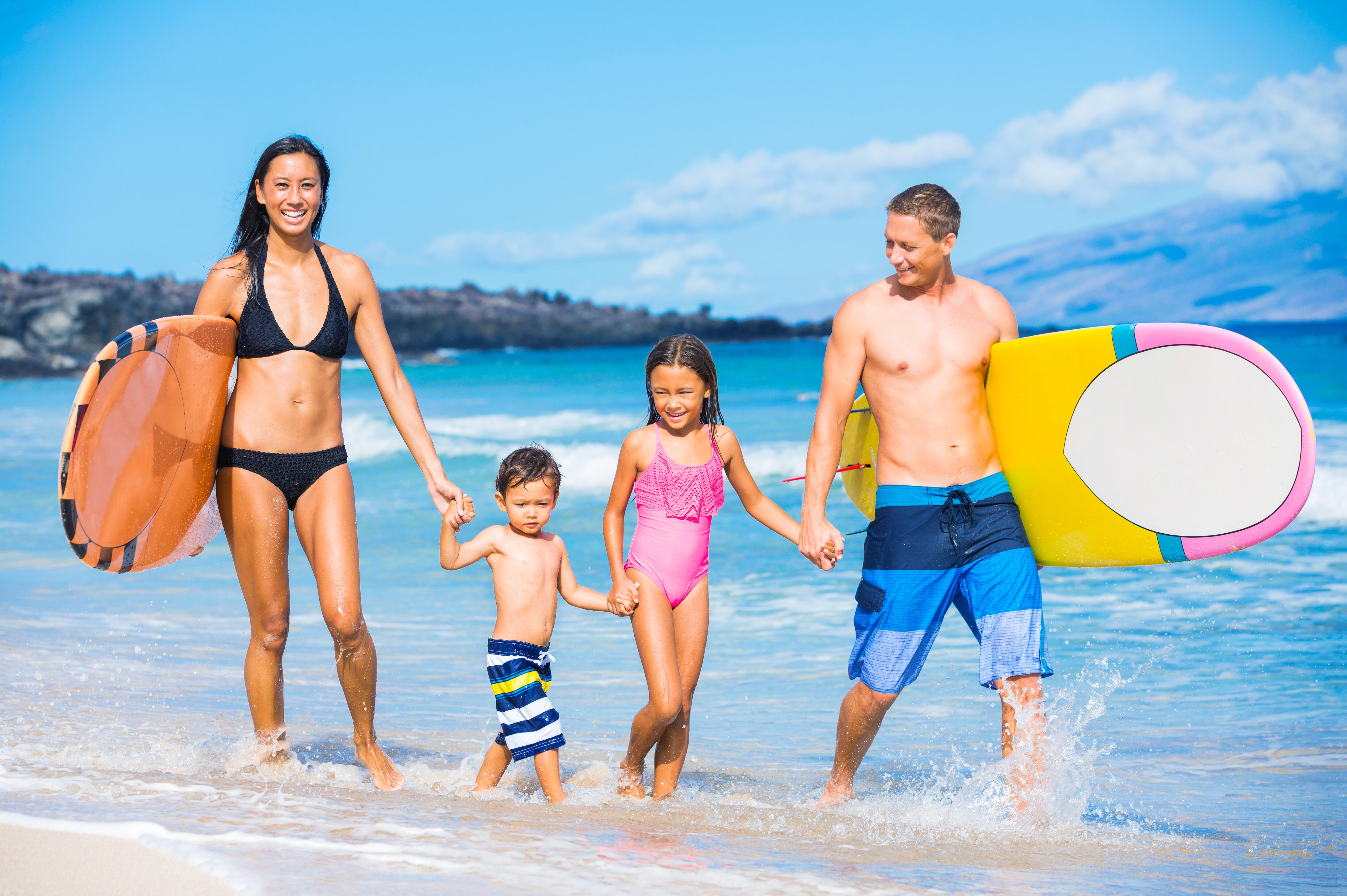 Family of four walking of the beach with surfboards