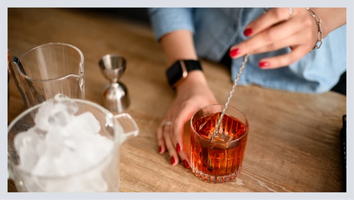 A closeup shot shows a cocktail being stirred, surrounded by cocktail-making tools.