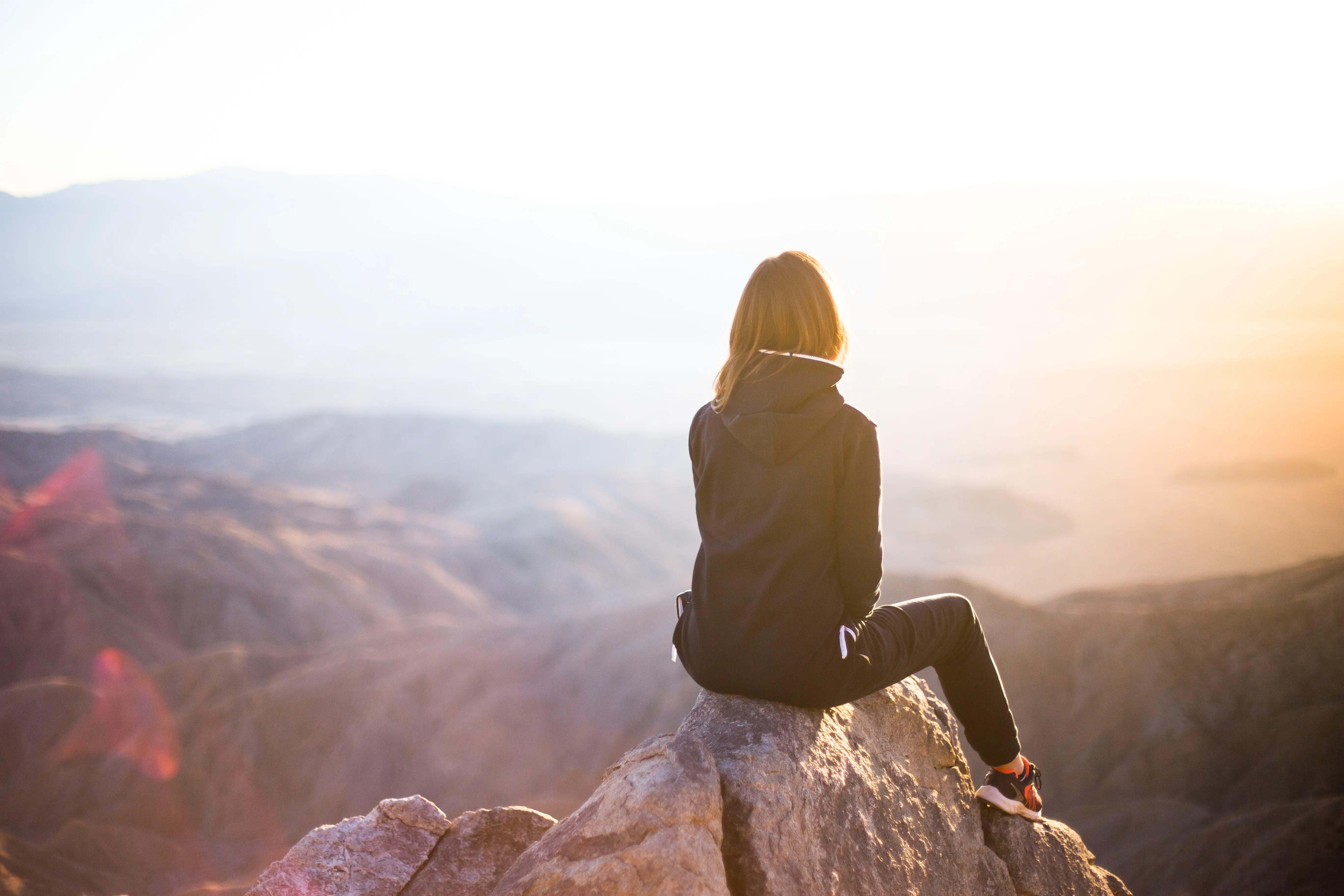 Image of a woman sitting on a rock and watching the sunset at Keys View in Joshua Tree National Park.