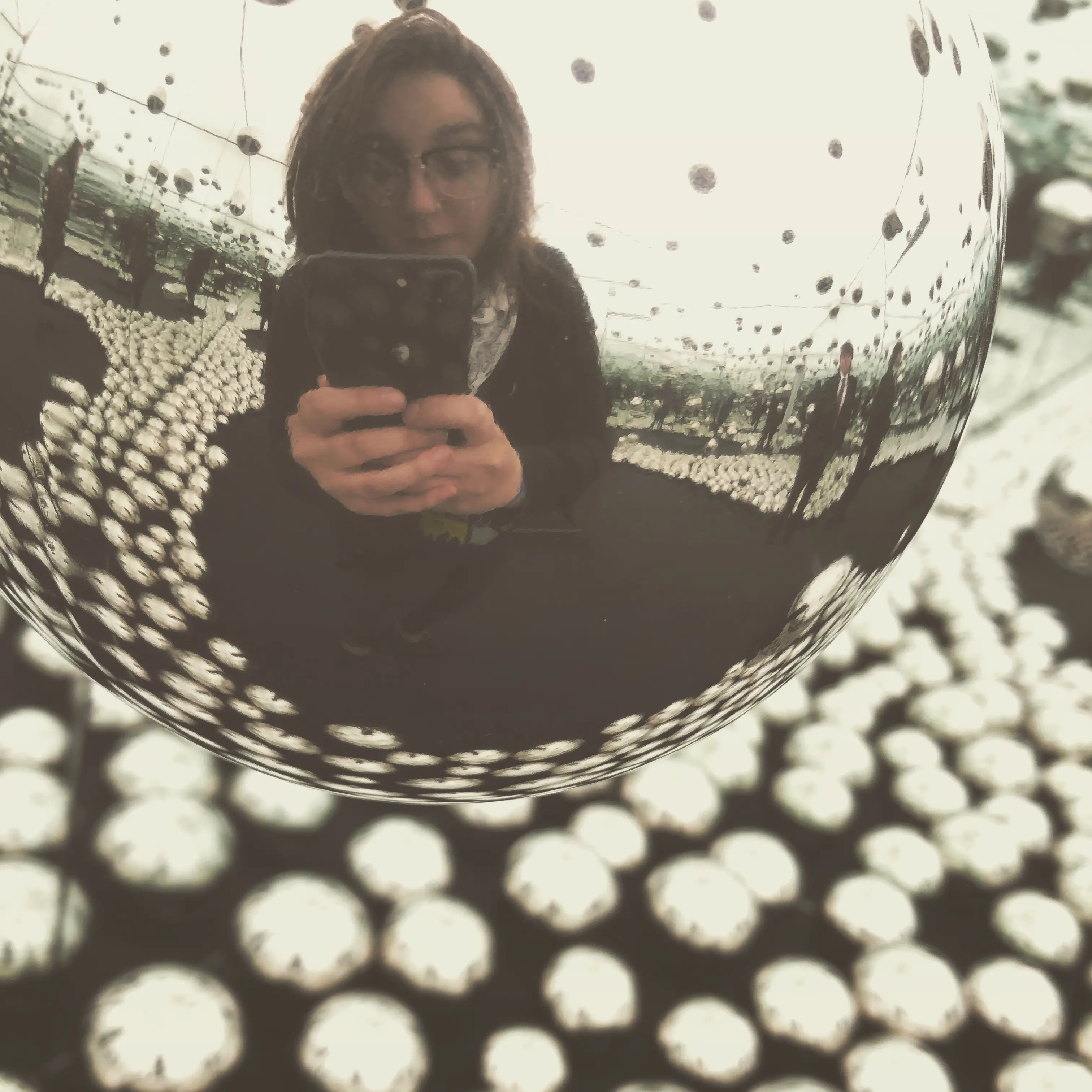 Image of a woman taking a selfie image in the reflection of an art display at WNDR Chicago.