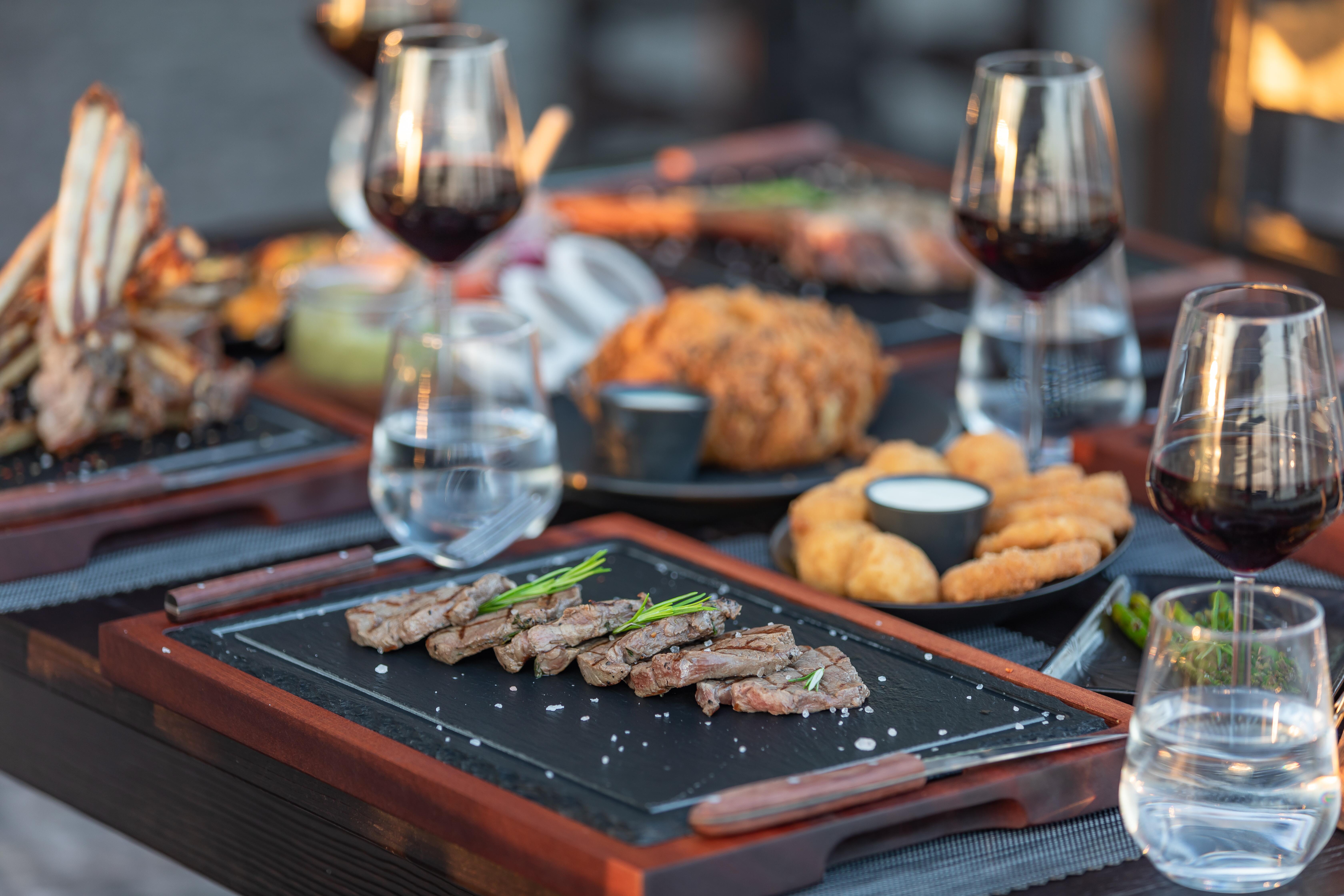Variety of meat dishes ready on outdoor table, with red wine at a luxury steakhouse restaurant