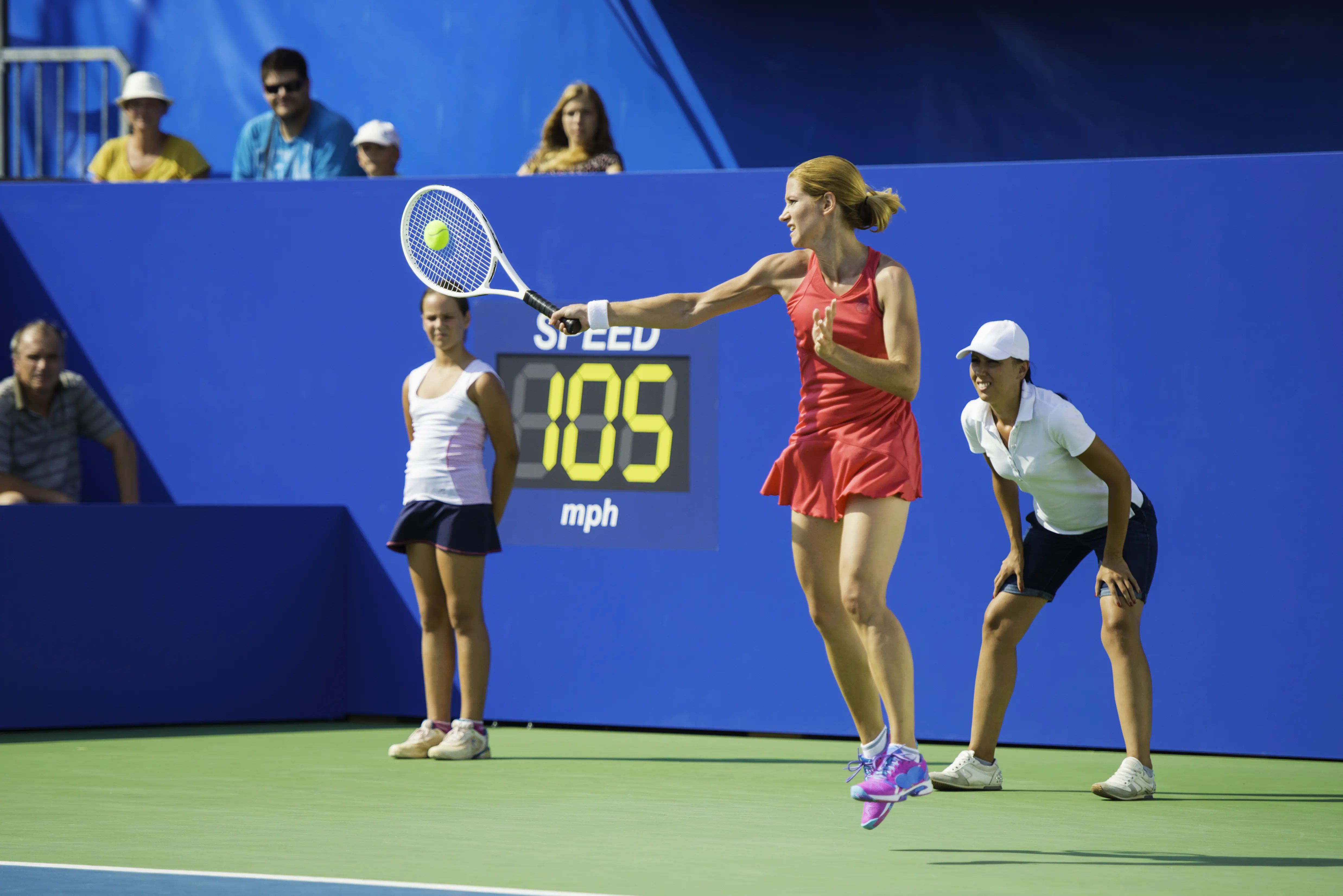 Female tennis player hitting forehand shot with spectators and ball kids in the background
