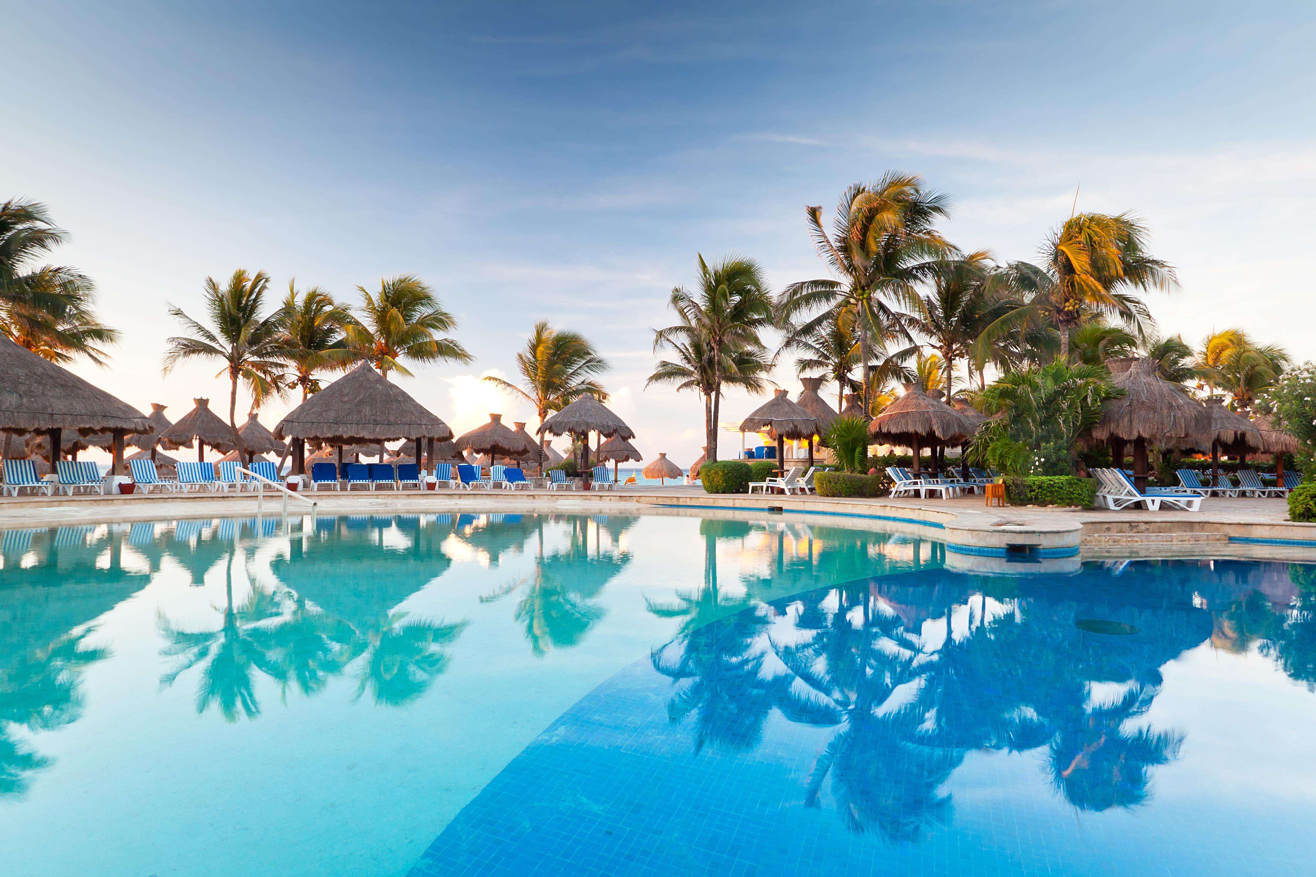 Tropical swimming pool at sunrise in Mexico, with blue stripe chairs and straw umbrellas