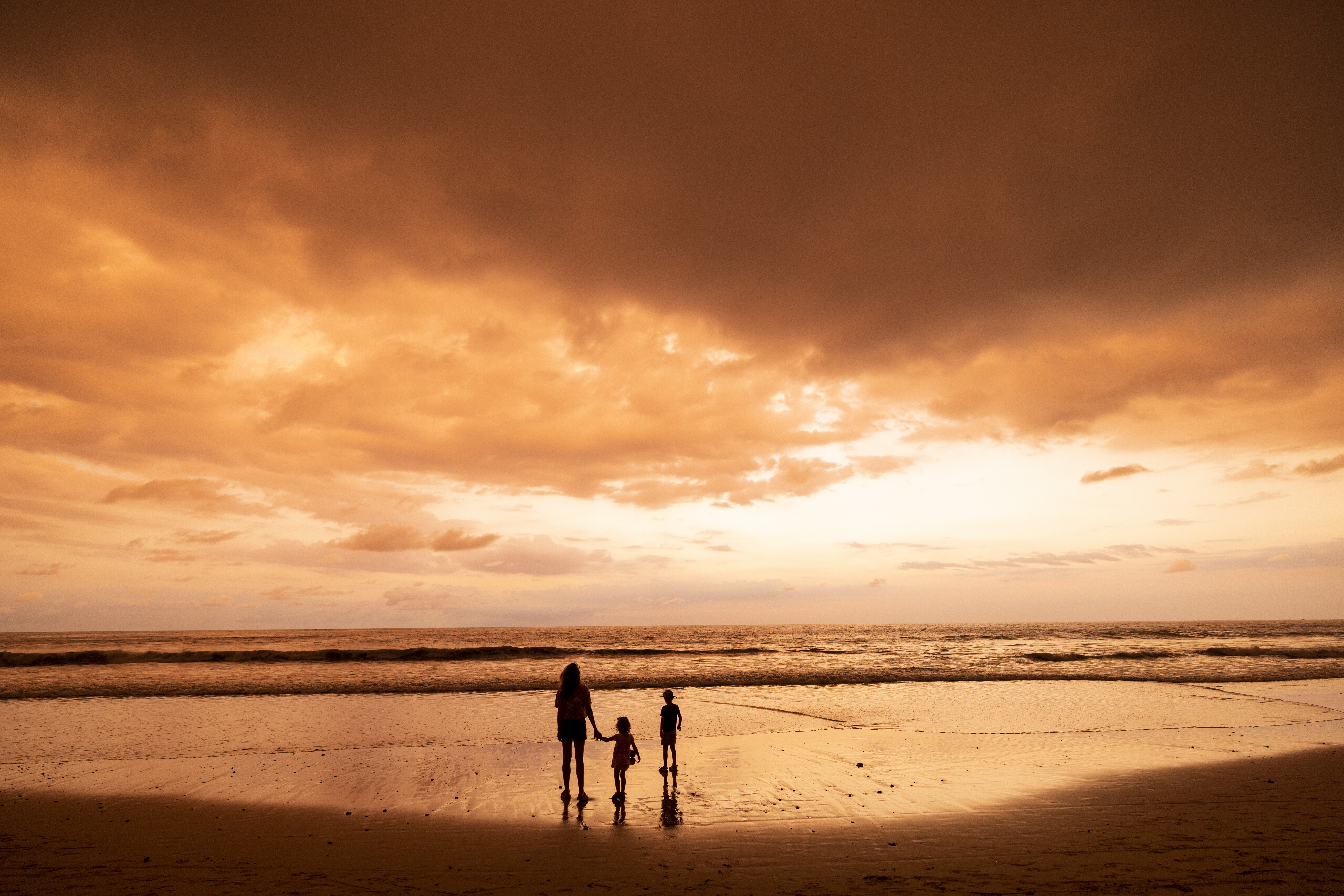 Silhouette image of a family standing in front of a beach sunset.