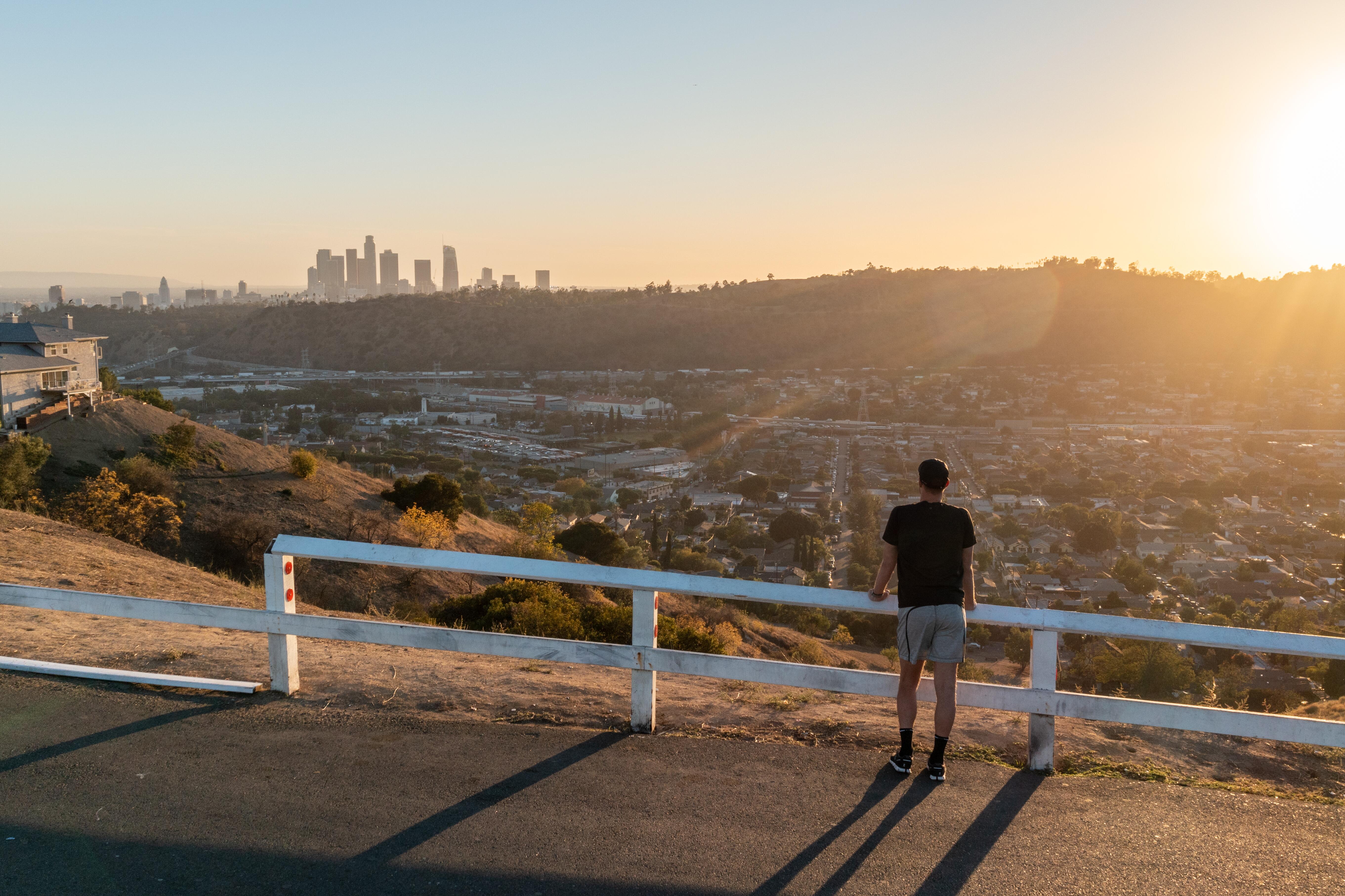 Image of a man looking at the city of Los Angeles in the distance, from a hiking trail.