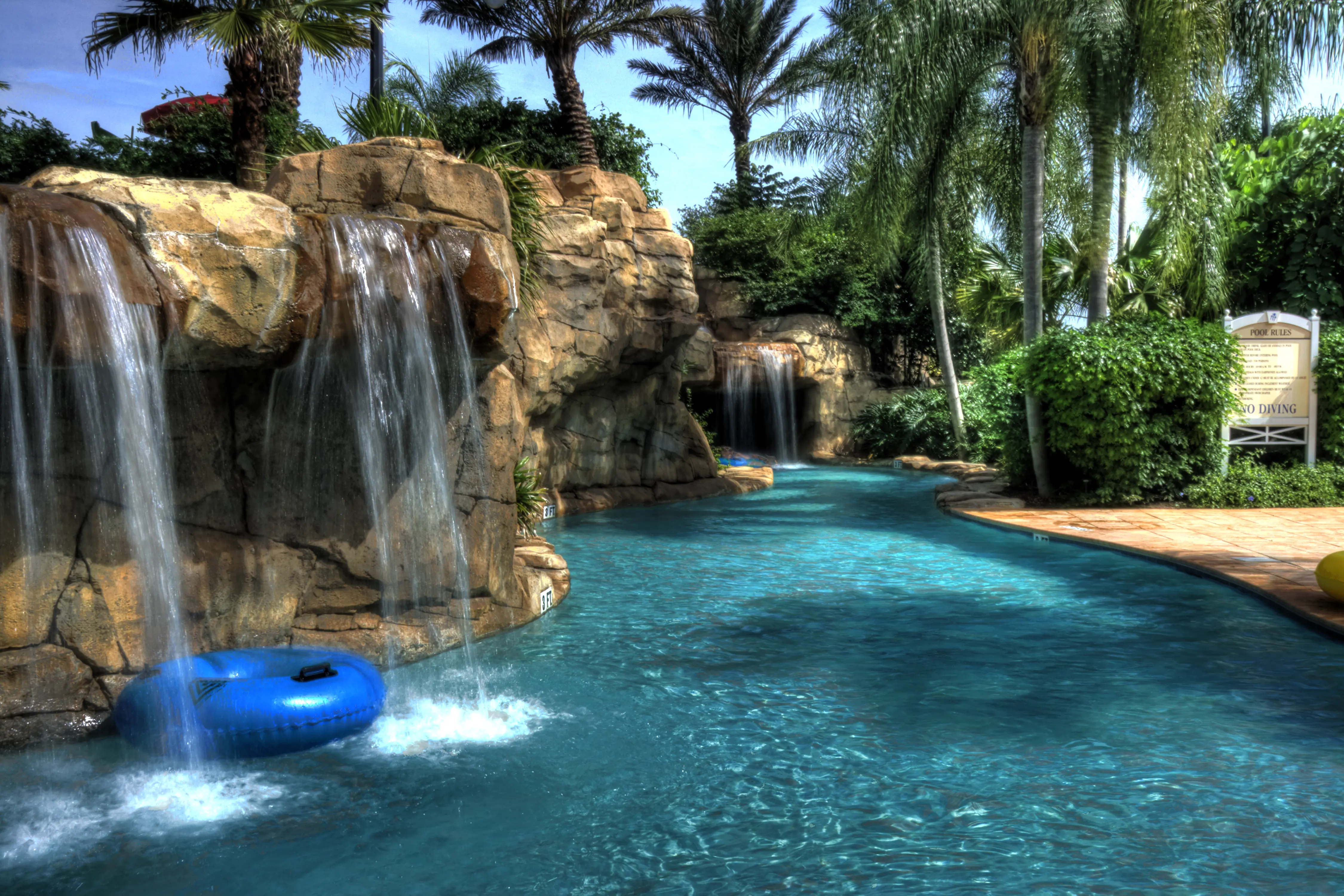 Resort or water park lazy river on sunny day with palm trees and water fall