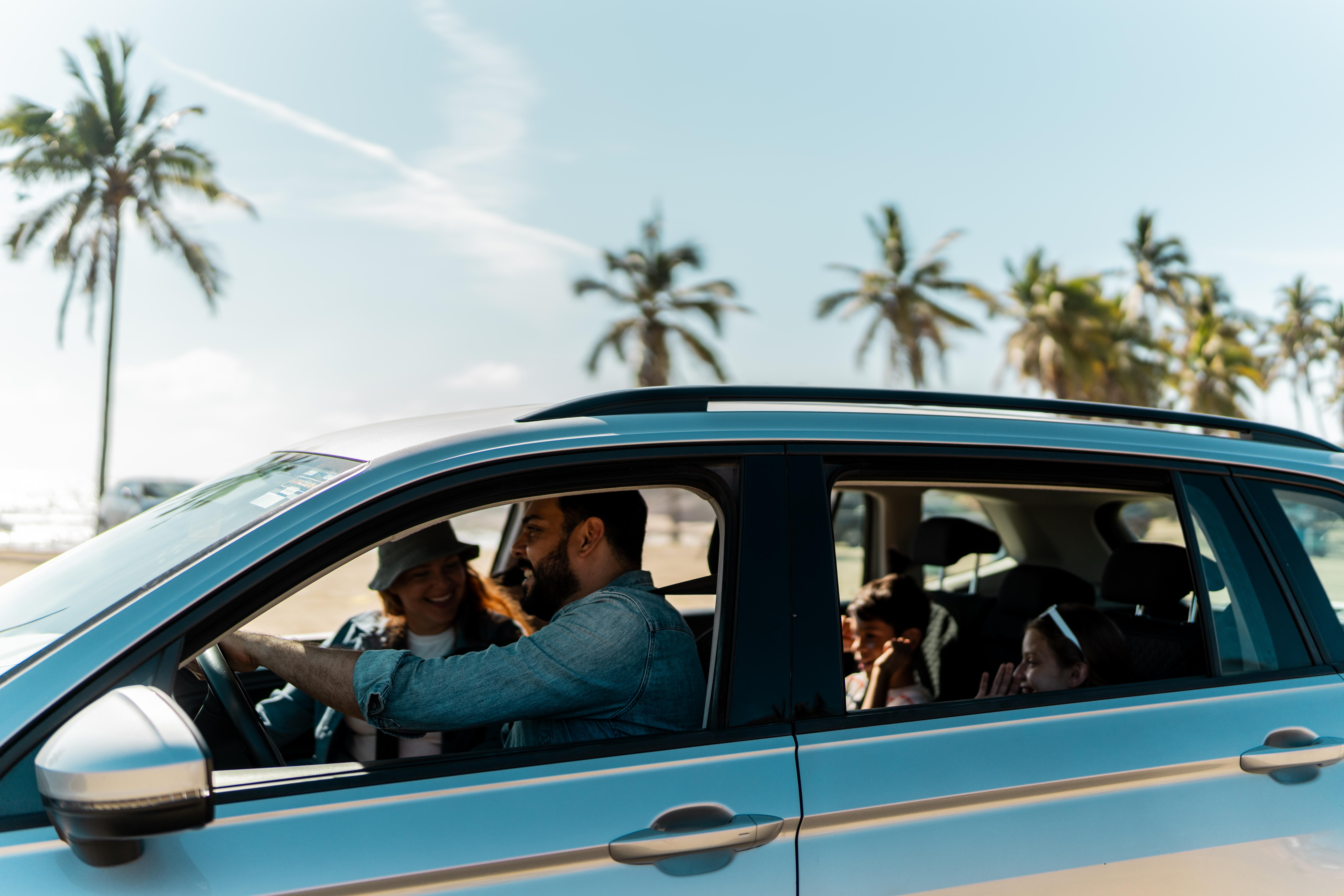 Father driving with family in car and palm trees in the background
