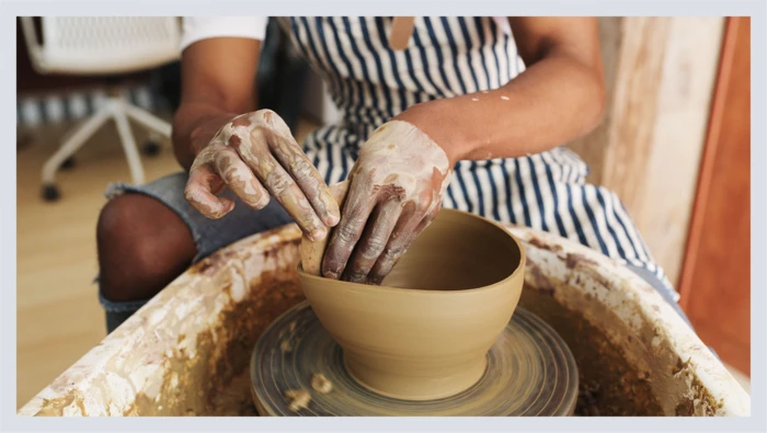 A person’s hands are shown spinning a piece of clay pottery on a pottery wheel.