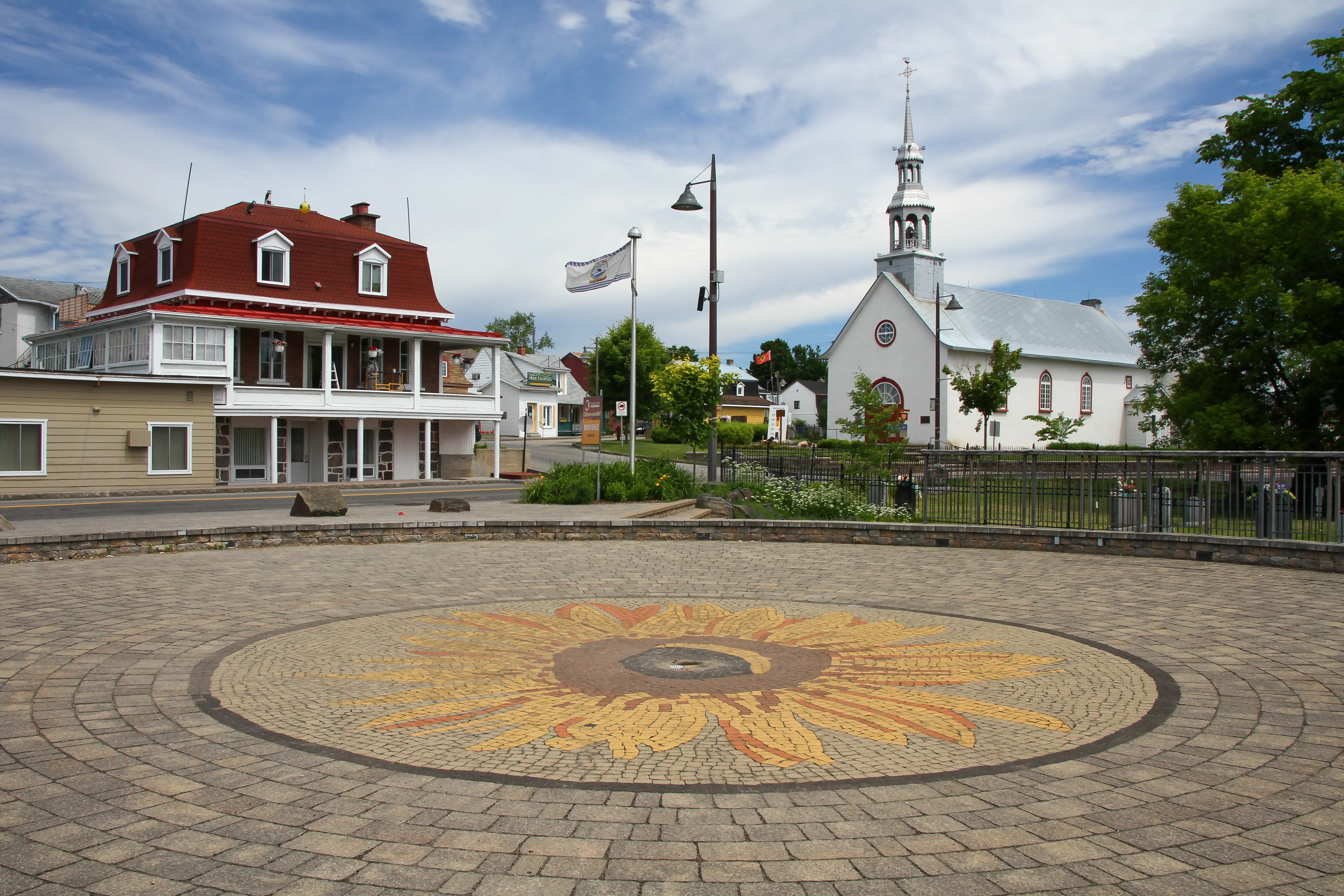 Image of the sunflower at the Huron-Wendat Nation Square in Wendake, with the Notre-Dame-de-Lorette chapel in the background.