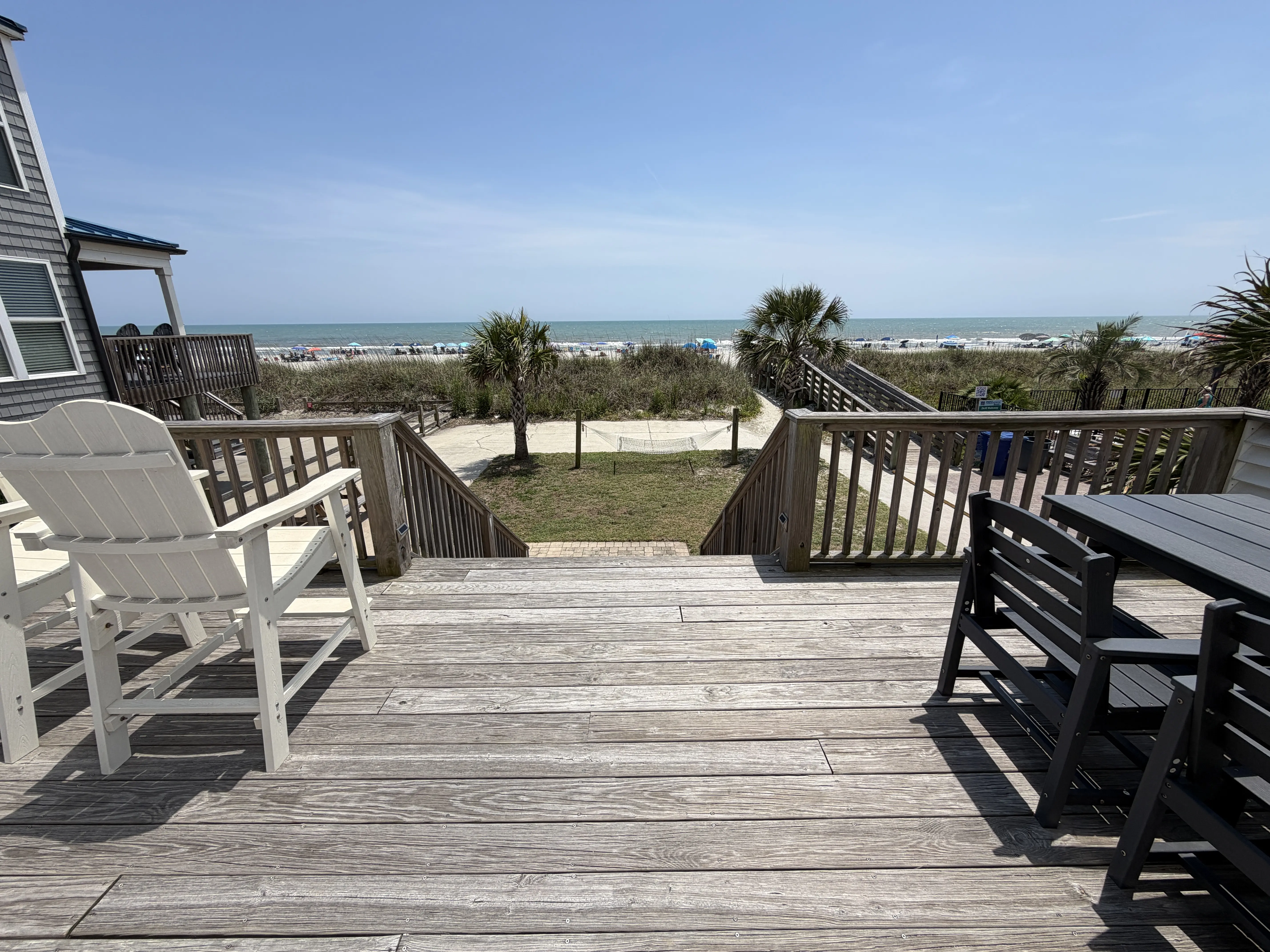 chairs and table sit on a raised wood patio that overlooks palm trees and Cherry Grove Beach in the background