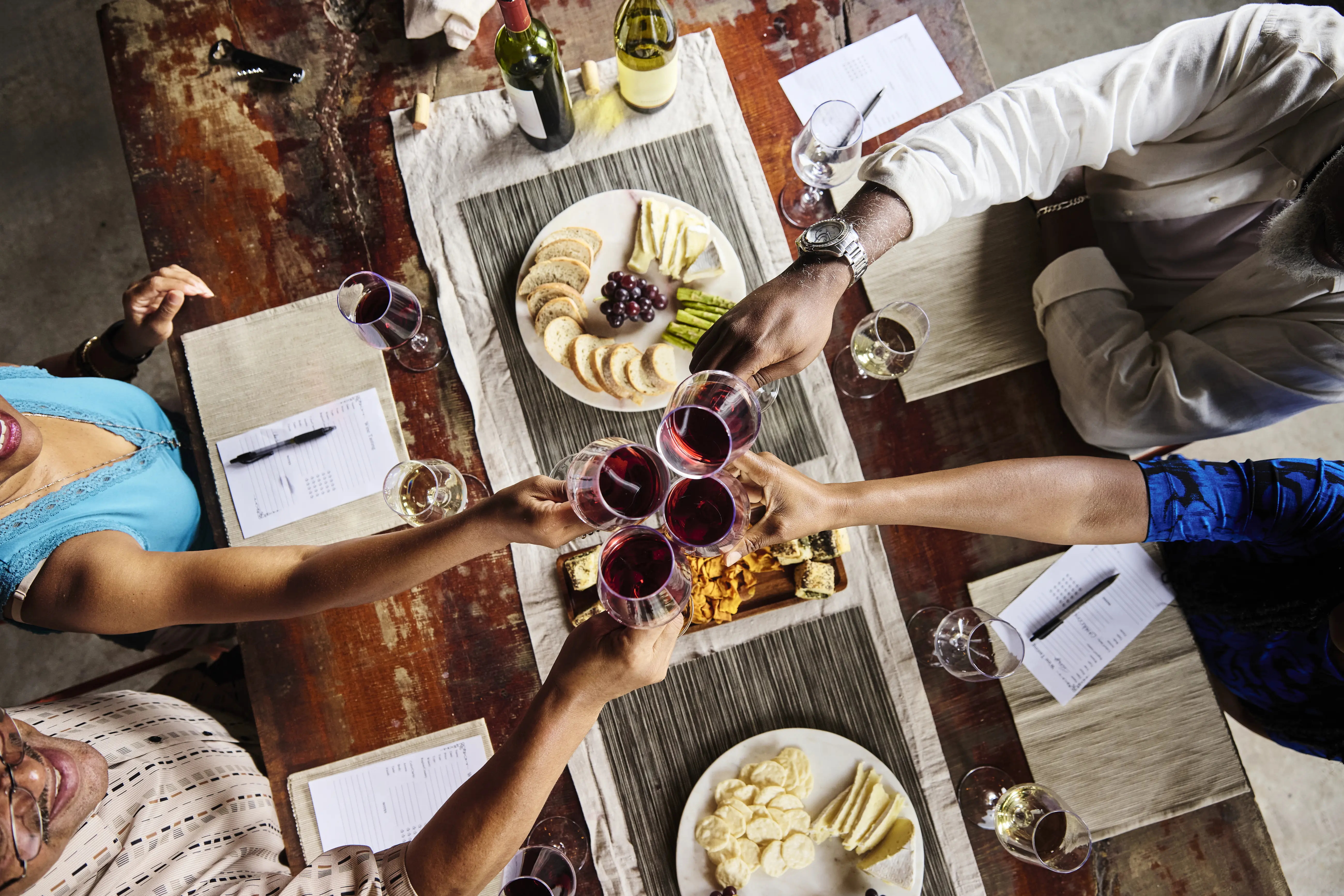 Overhead image of four friends sitting at a dinner table, toasting with wine glasses.