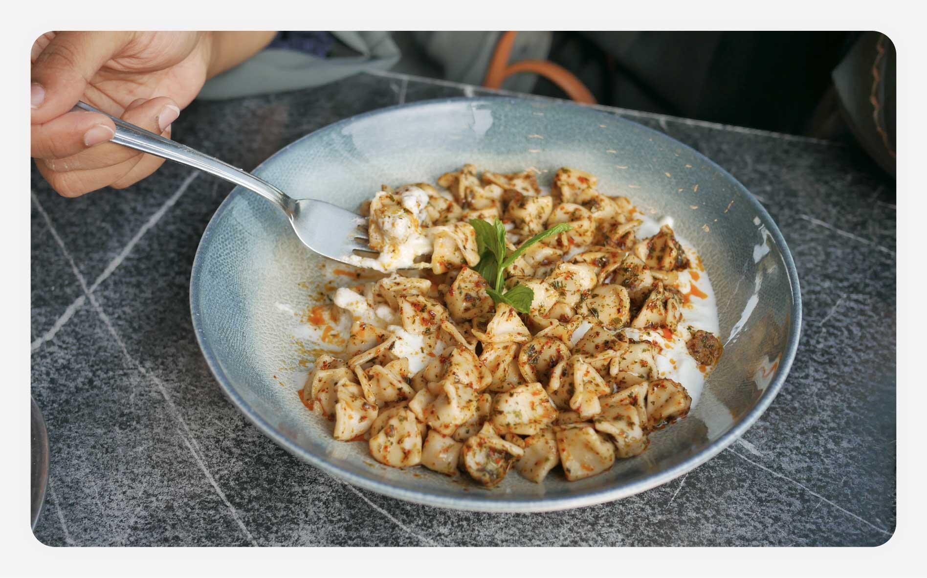 Someone eating a bowl of Turkish dumplings.
