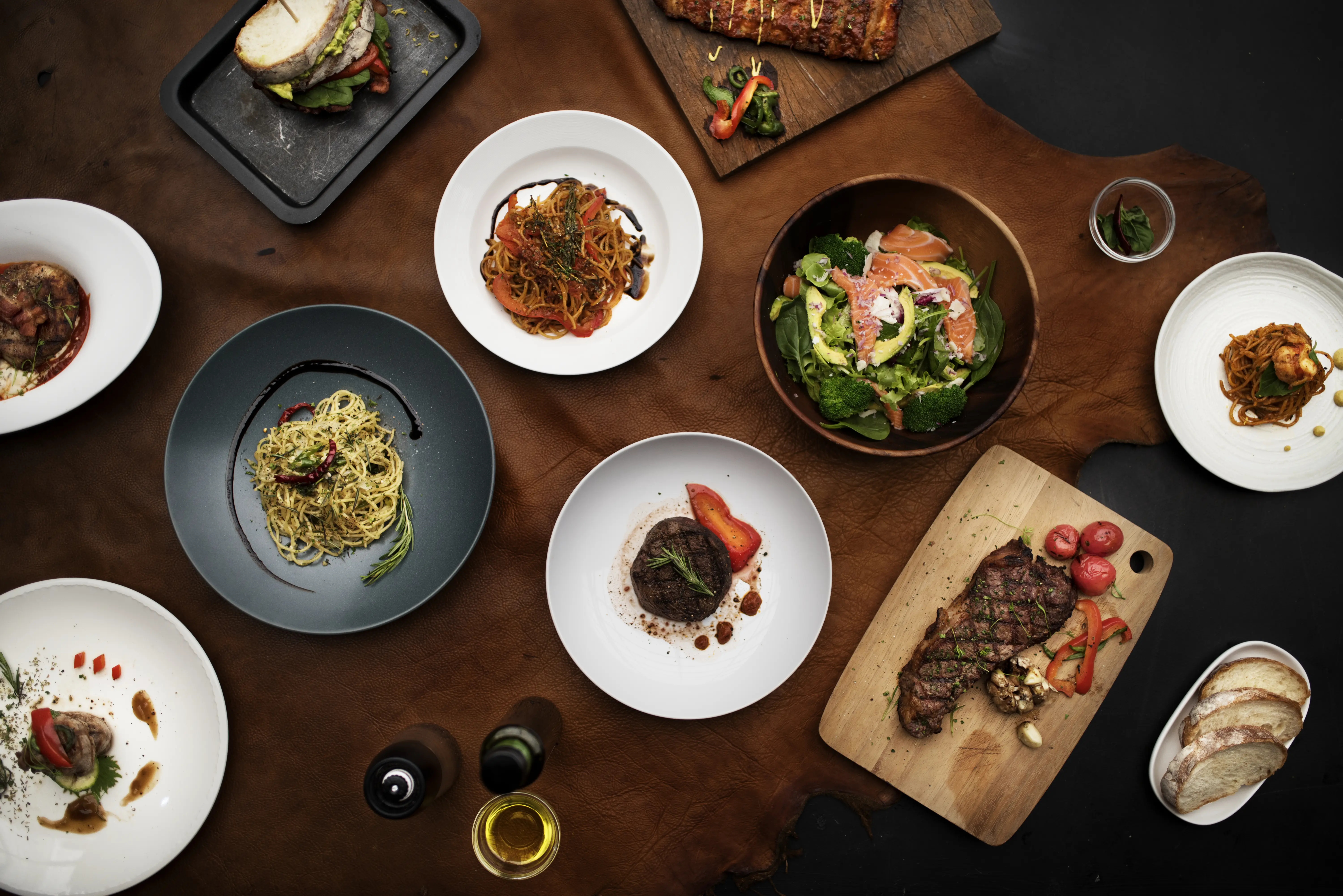 Variety of western style dishes featuring bread, meat, fish and pasta with touches of red peppers on a wood table, aerial view