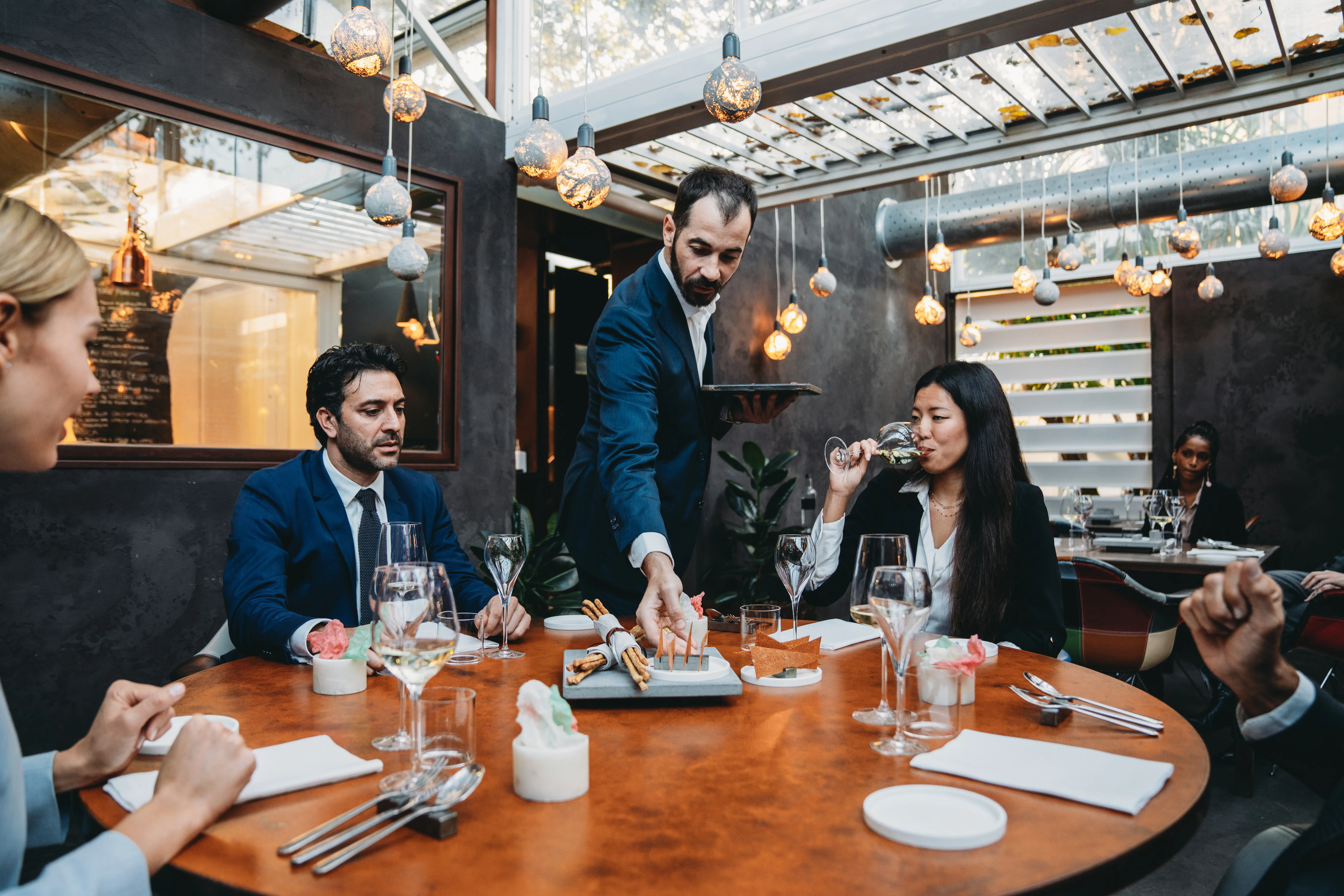 Image of a waiter serving appetizers to a table of guests in a fancy restaurant.