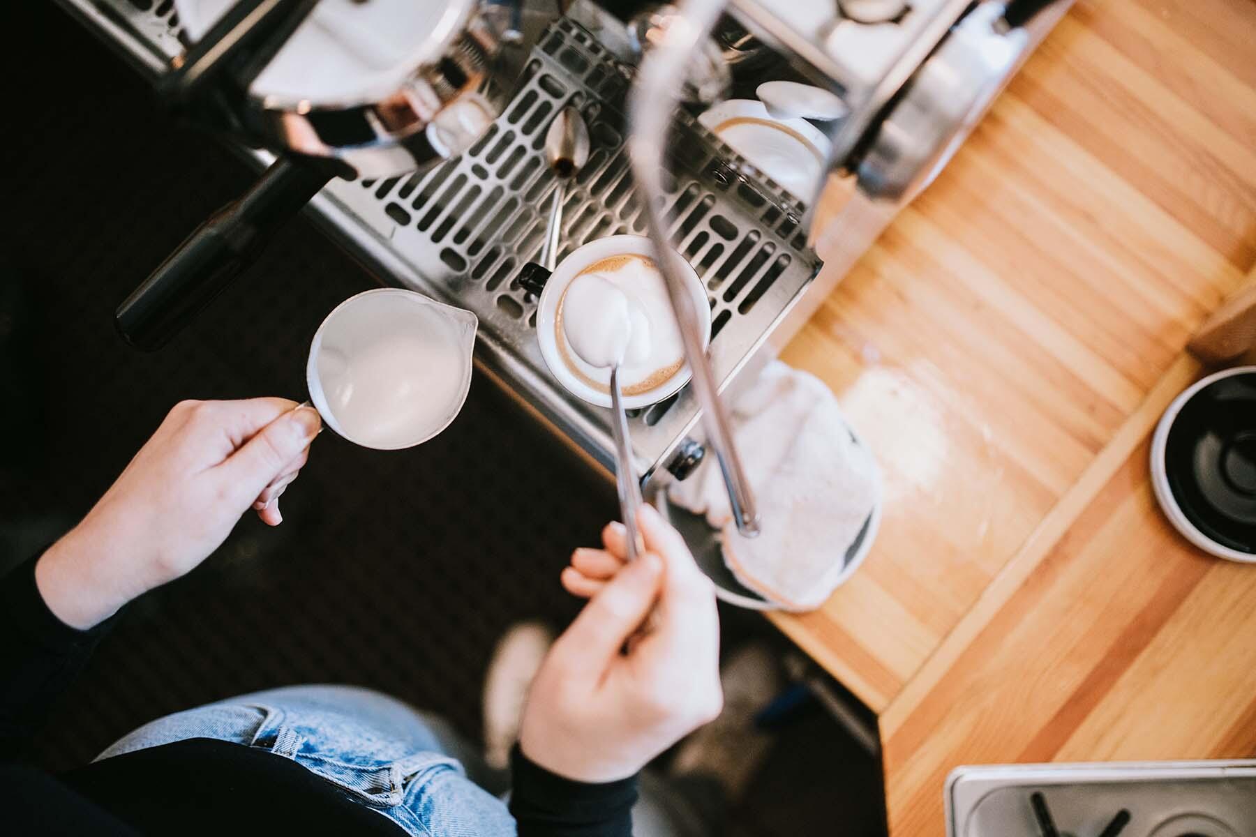 A barista frothing milk for a latte in a coffee shop