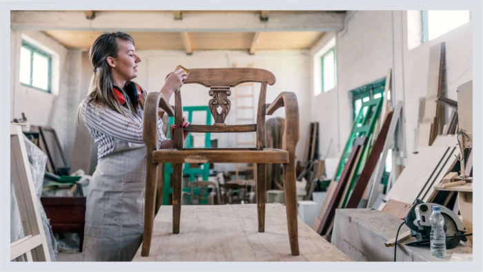 A woman works on restoring an old chair in a workshop during a furniture restoration class. 