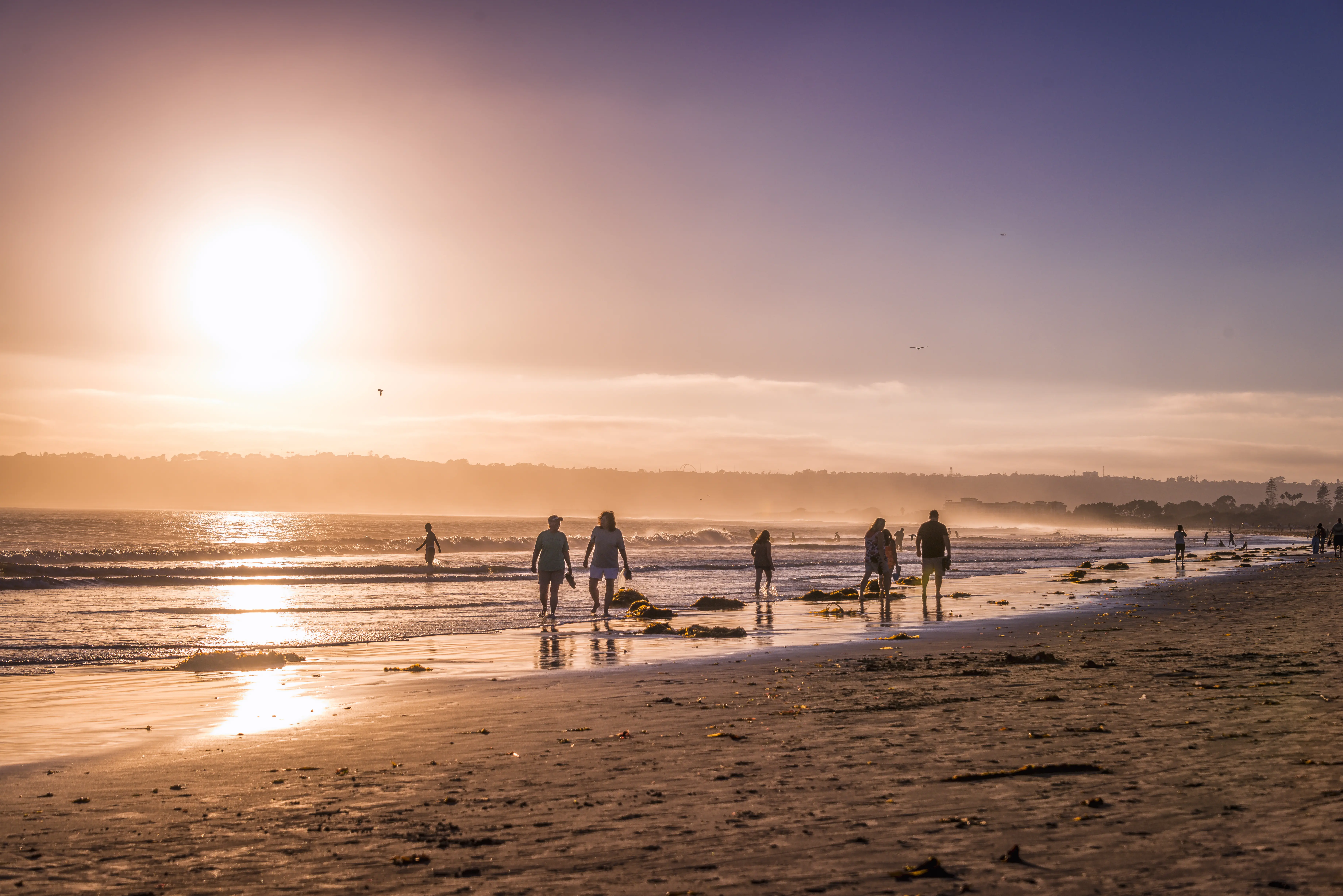Image of people walking on a California beach during sunset.