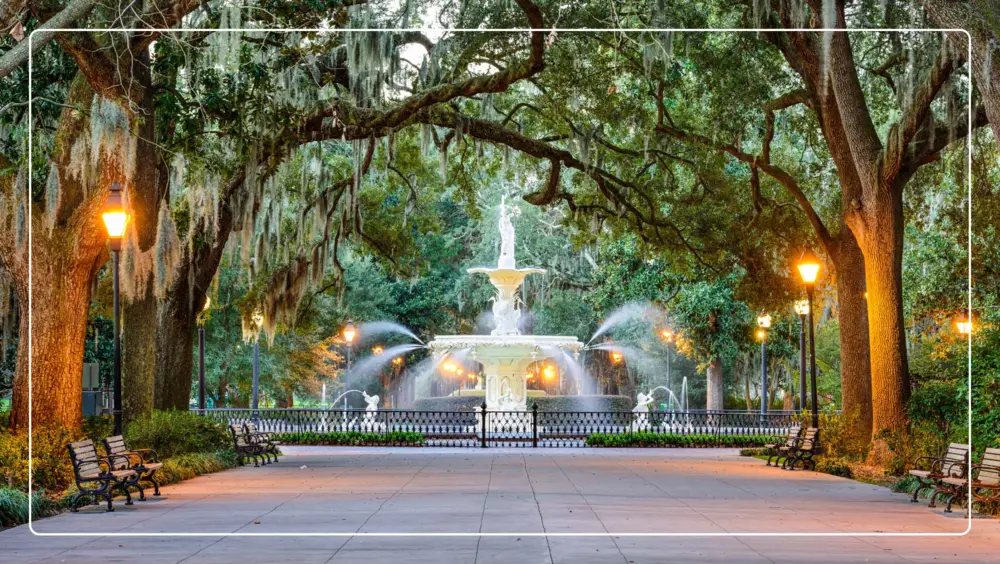 A tree-lined street in Savannah with a fountain in the background.