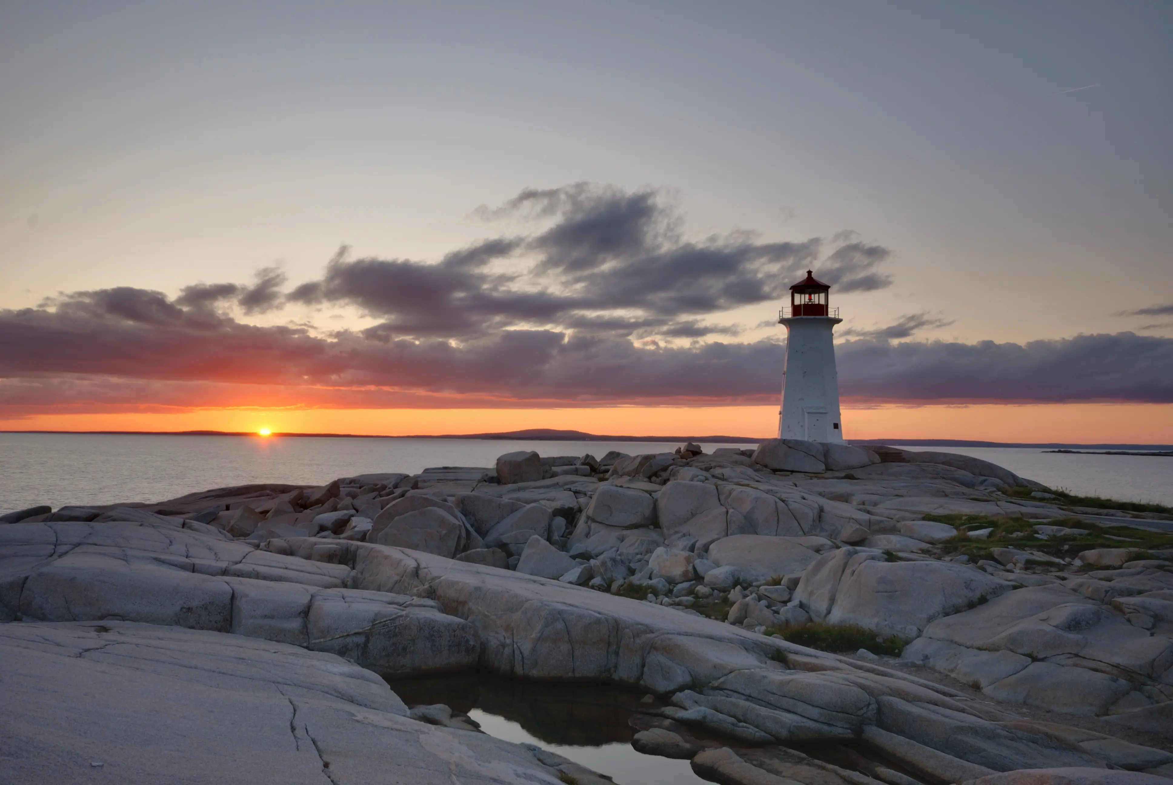 Scenic outdoor image of Peggy’s Cove with ocean and sunset in the background.