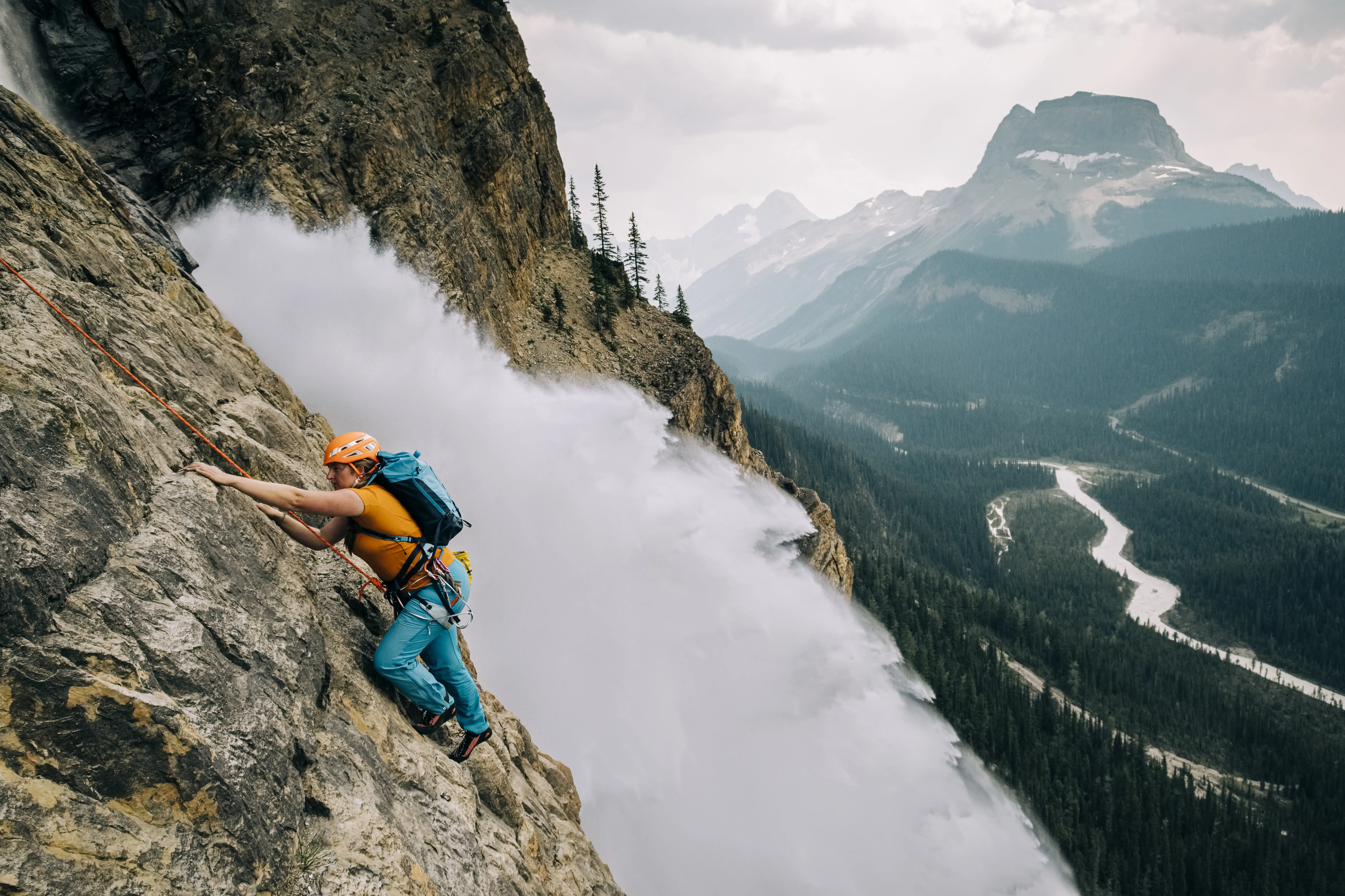 Image of a female rock climber climbing beside a dramatic waterfall in Yoho National Park.