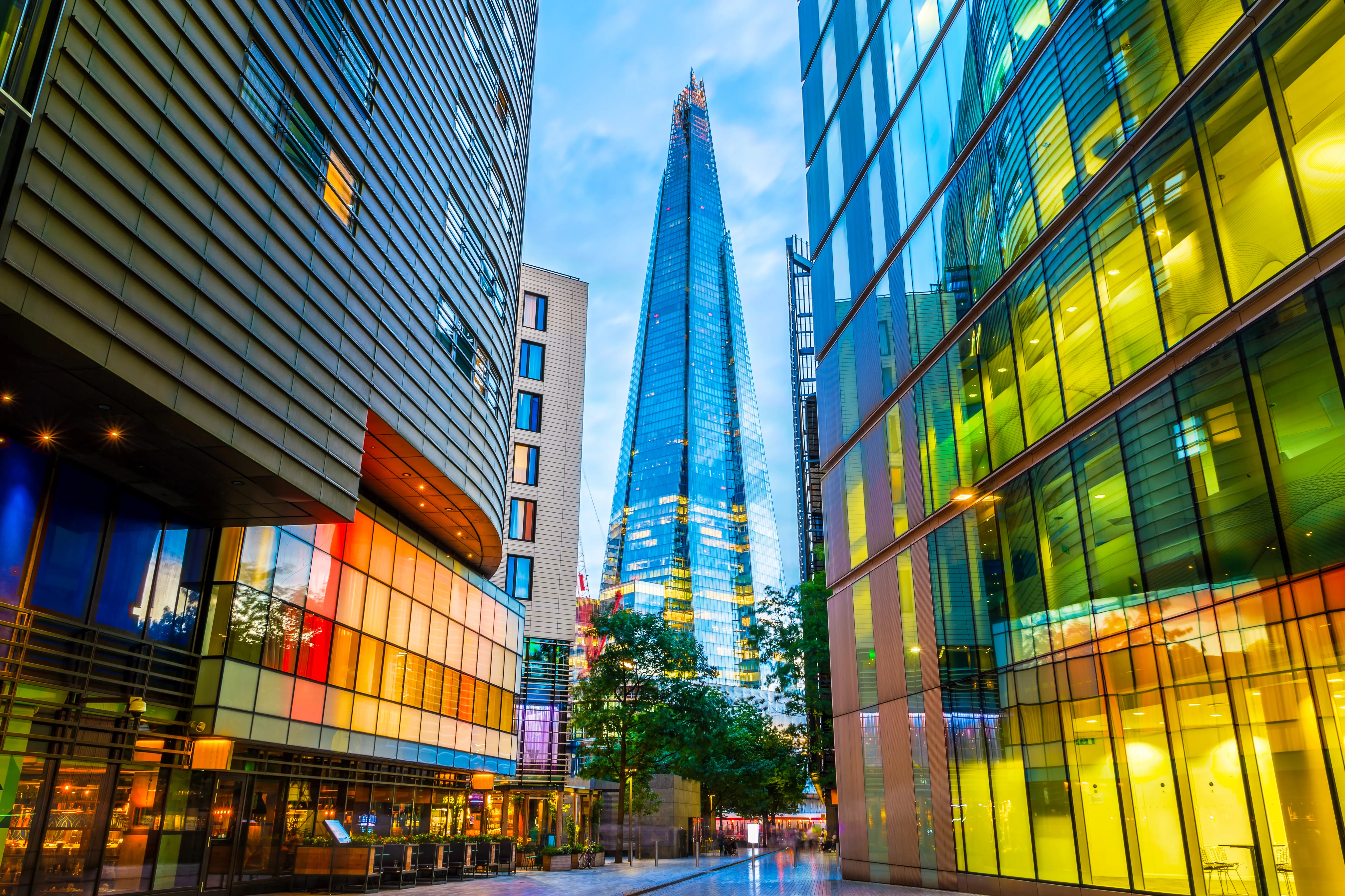 Street view of modern buildings with colorful lights in London, showing The Shard skyscraper in background