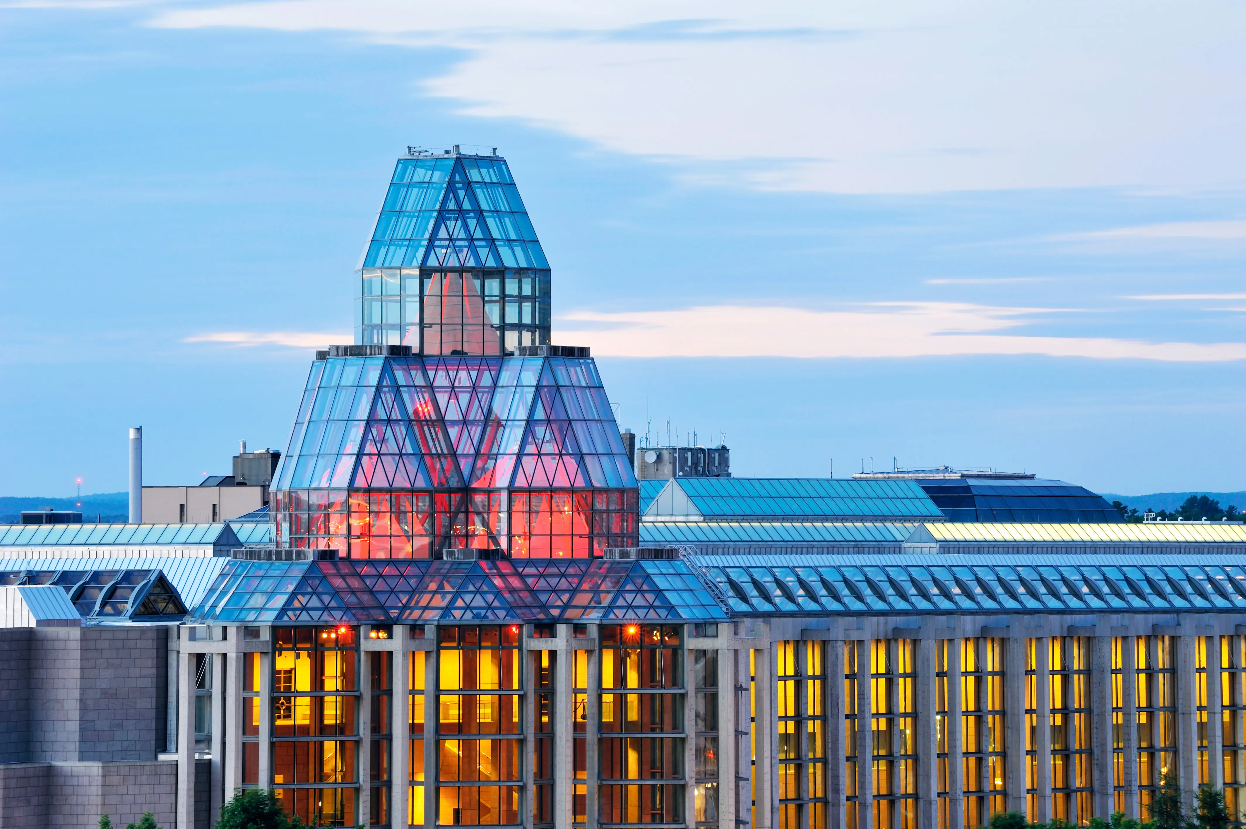 The National Gallery shown in the evening with neoclassical architecture featuring a blend of glass, granite, and concrete lit with pink and yellow hues
