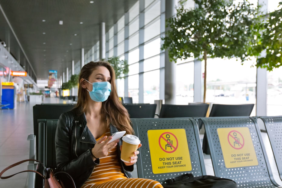 Girl sitting at airport gate waiting area with a face mask on.