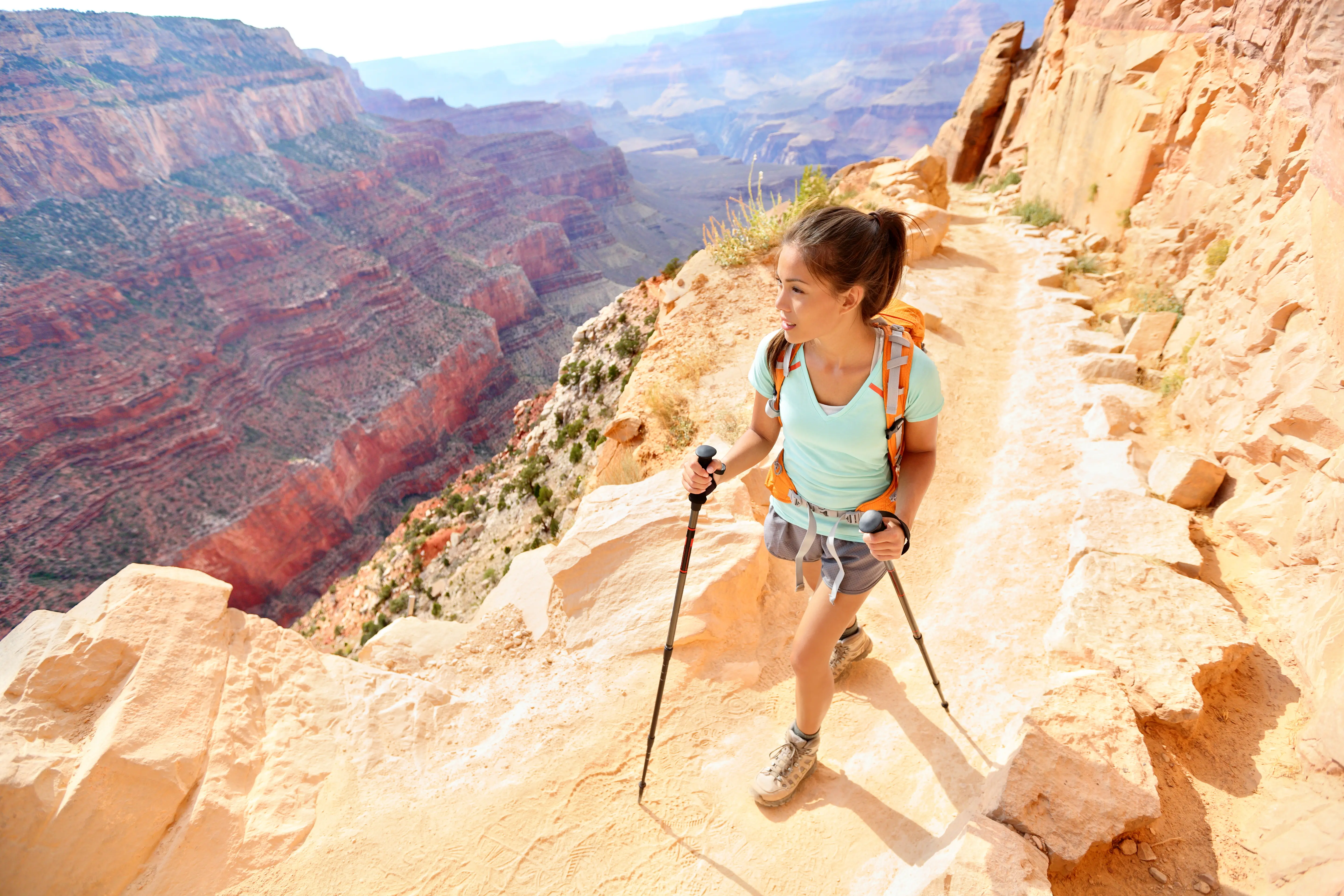 Female hiker in Grand Canyon South Rim walking on cliffside trail with hiking poles, Arizona, USA