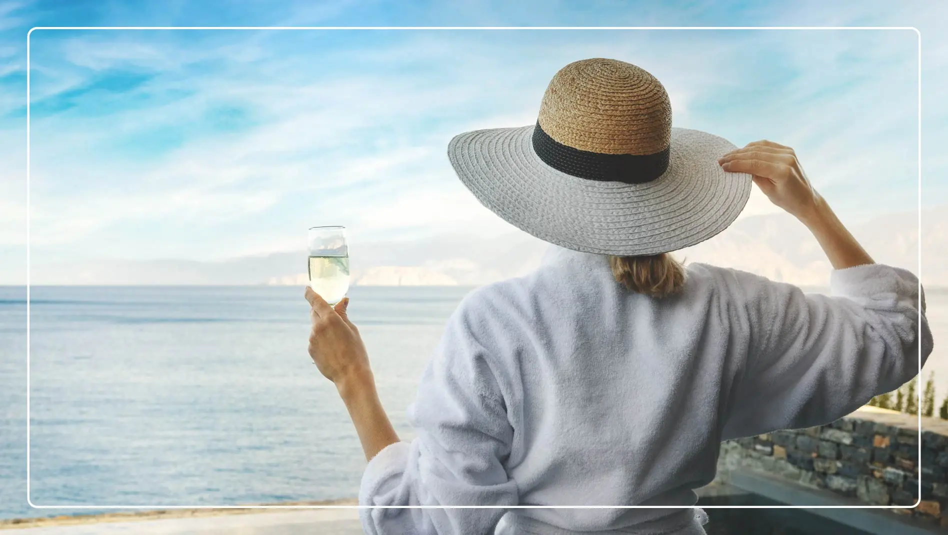 A woman in a bathrobe holds a glass of champagne while looking out at the ocean in Los Cabos, Mexico.