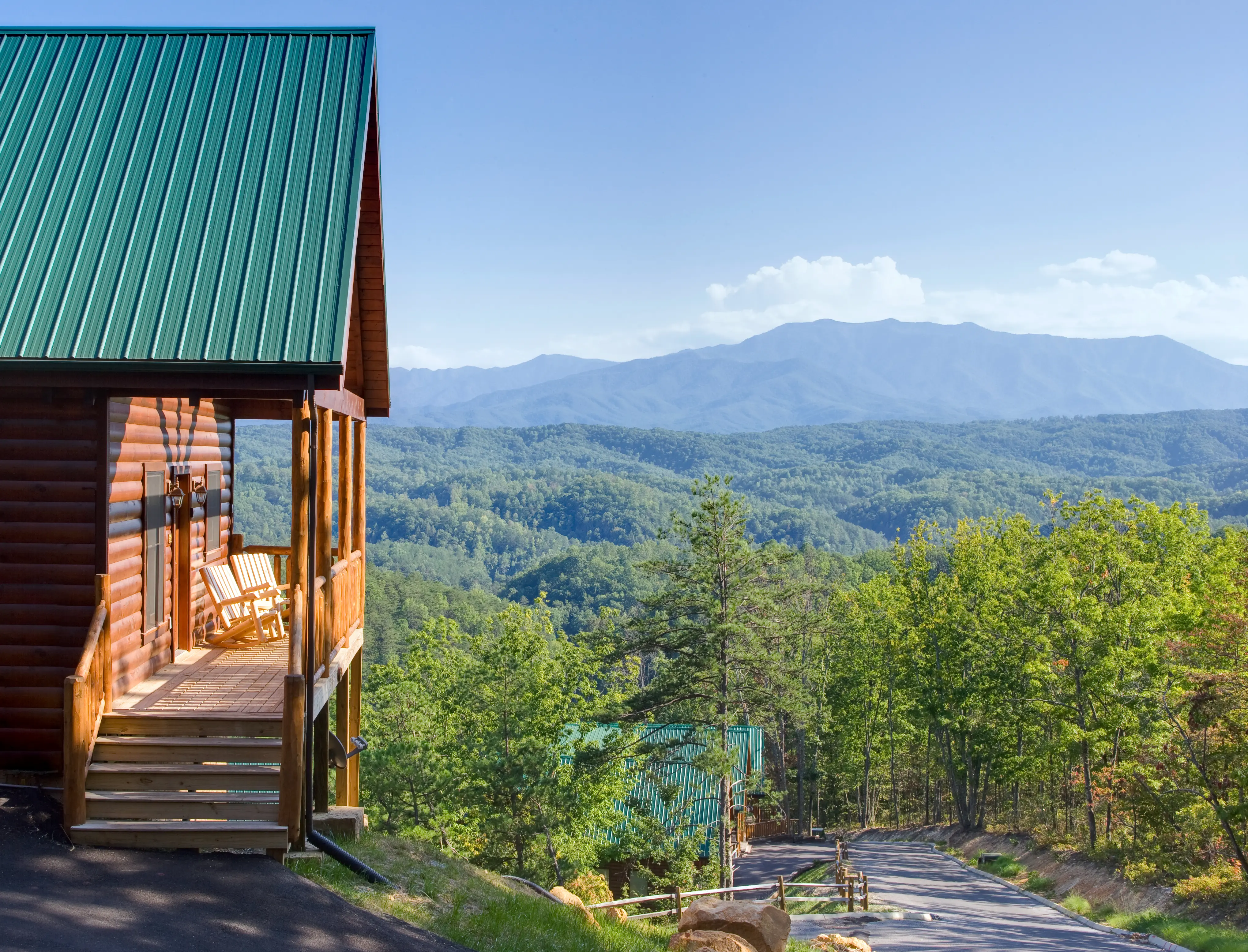Mountain side cabins with green metal roof and grand view of the Smoky Mountains on a sunny day