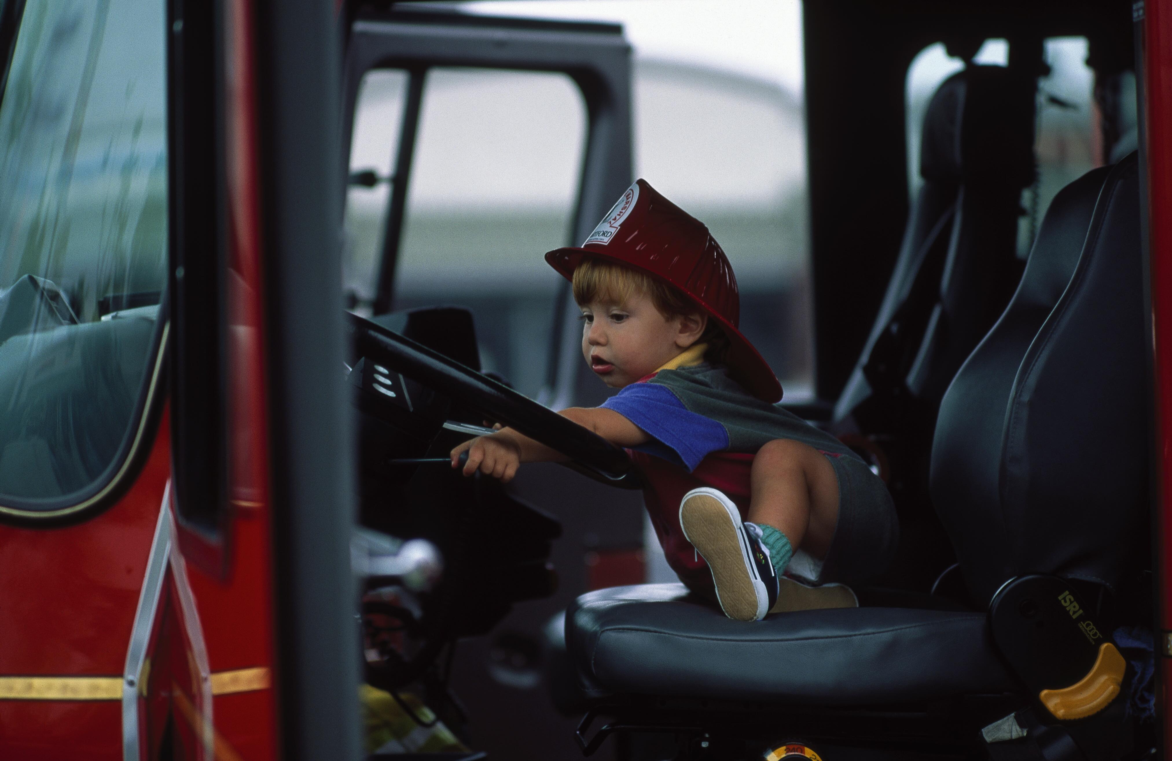 Image of a toddler in a fire helmet sitting in a fire truck.