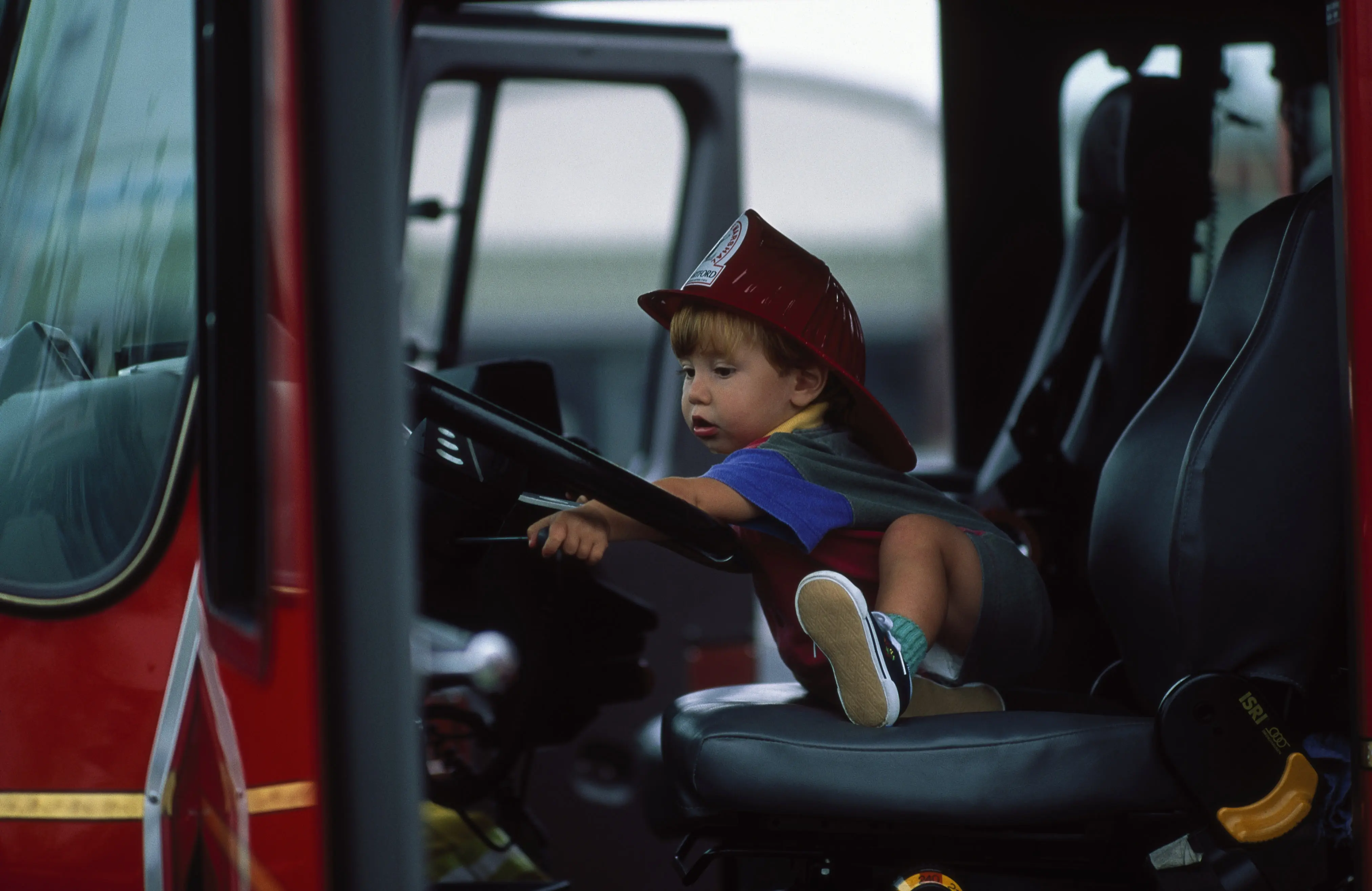 Image of a toddler in a fire helmet sitting in a fire truck.