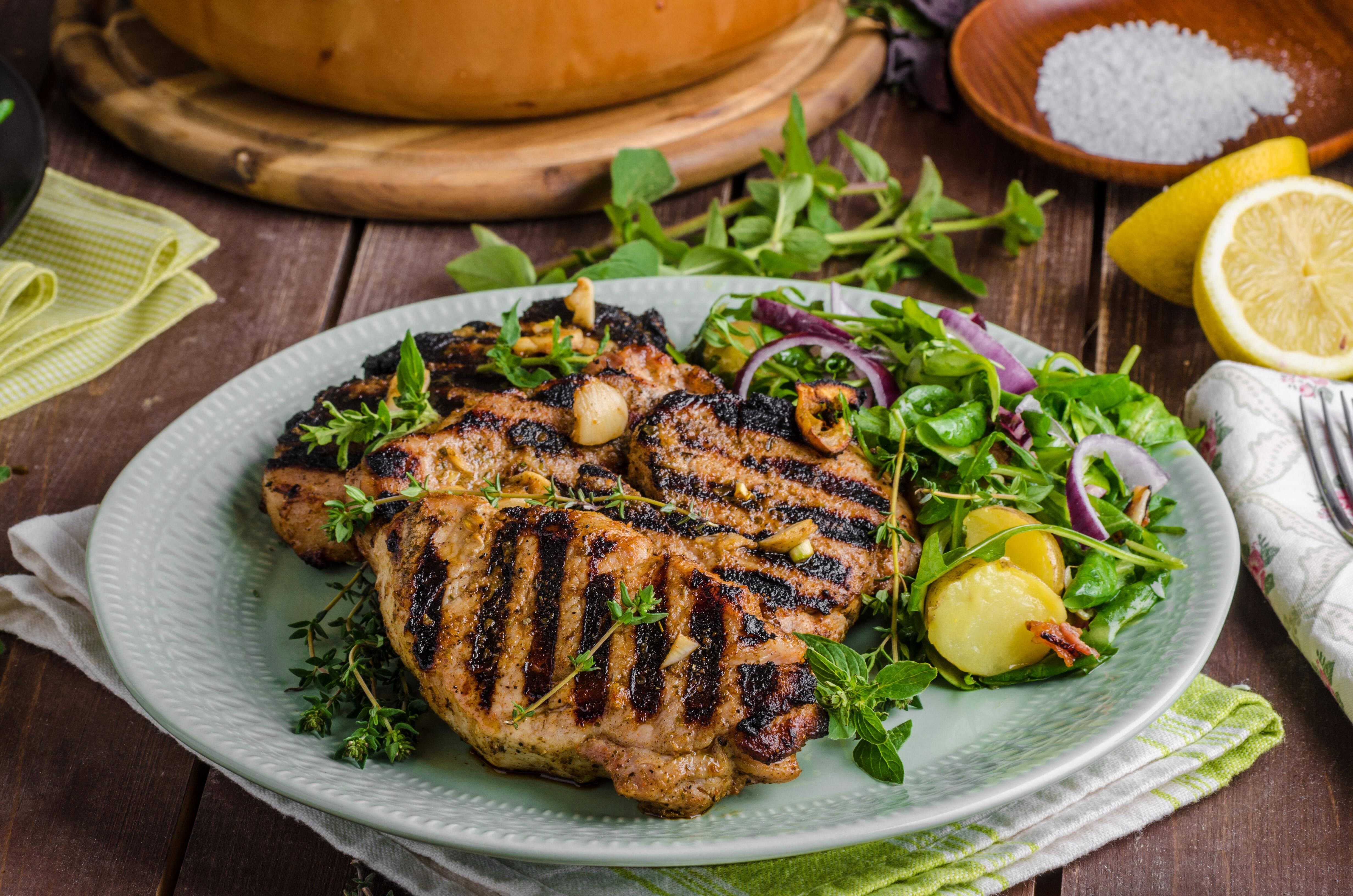 Grilled pork chops with lettuce salad and lemon, set in white plate on a wood table