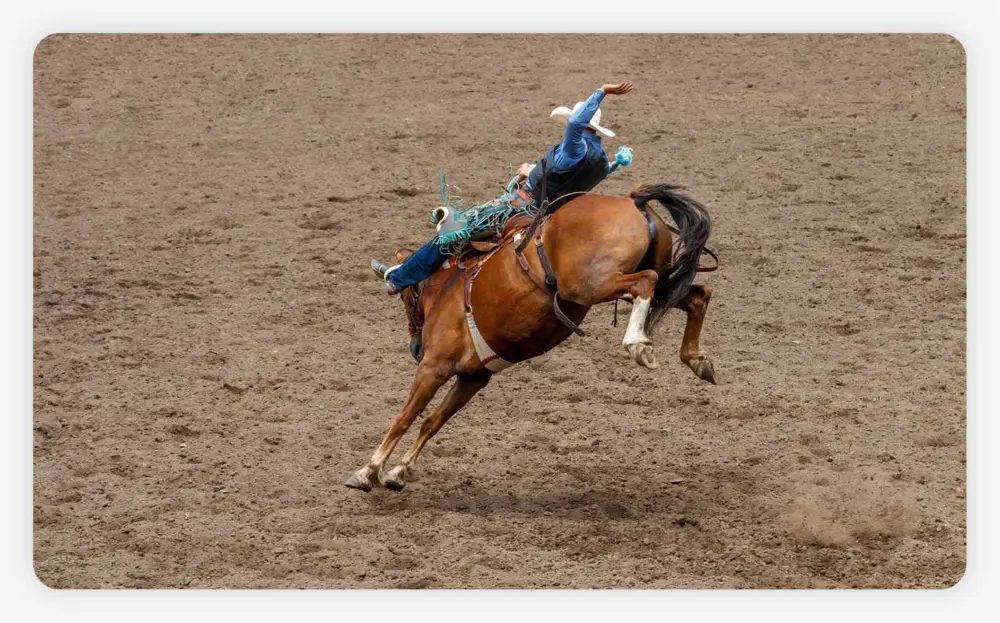 A cowboy is riding a bucking bronco at a rodeo in an arena