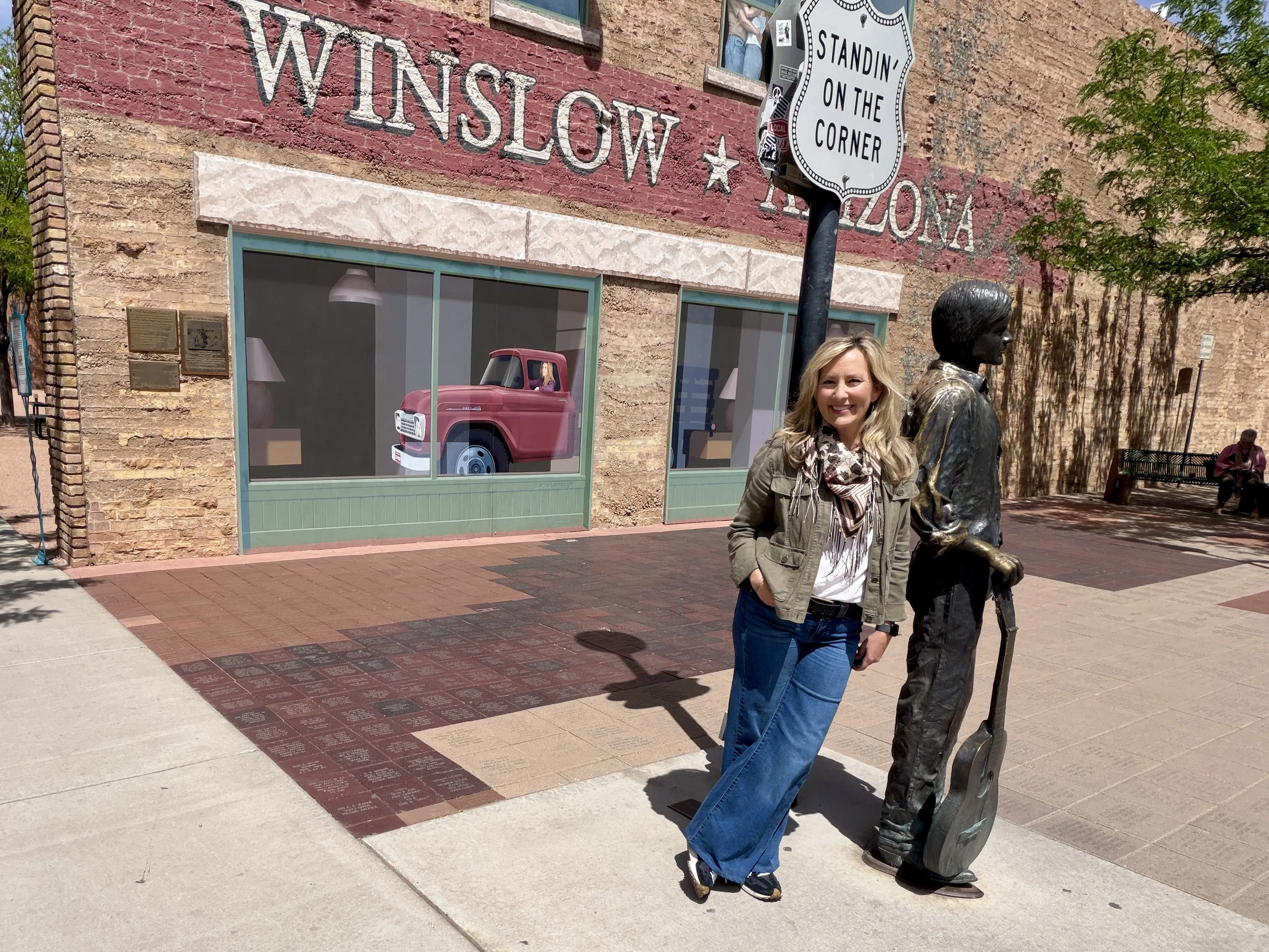 Woman with long blonde hair leans against sign post next to metal statue of a man holding a guitar