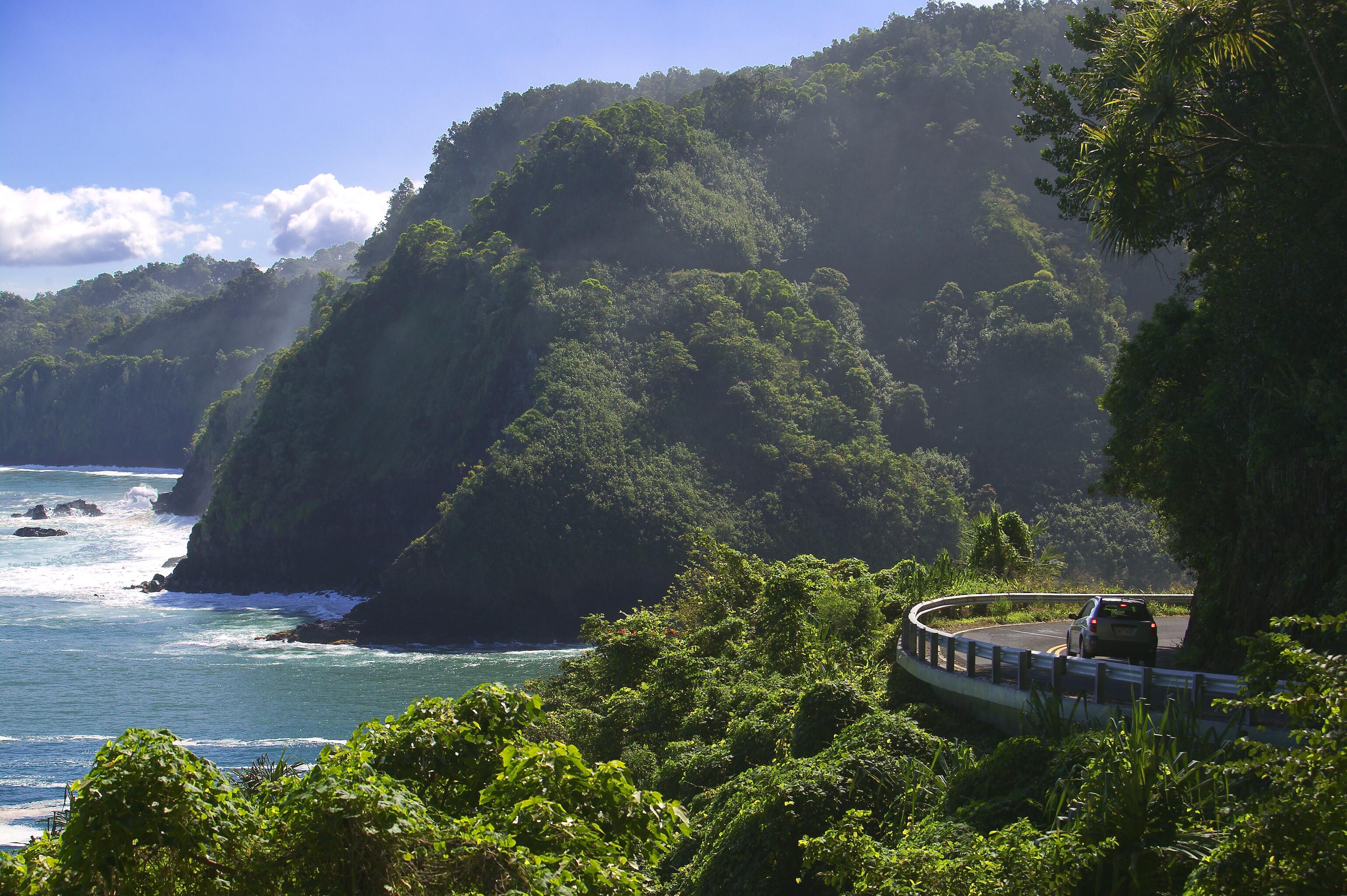 Road winding around the sea cliffs with powerful ocean waves creating a misty spray in Maui, Hawaii