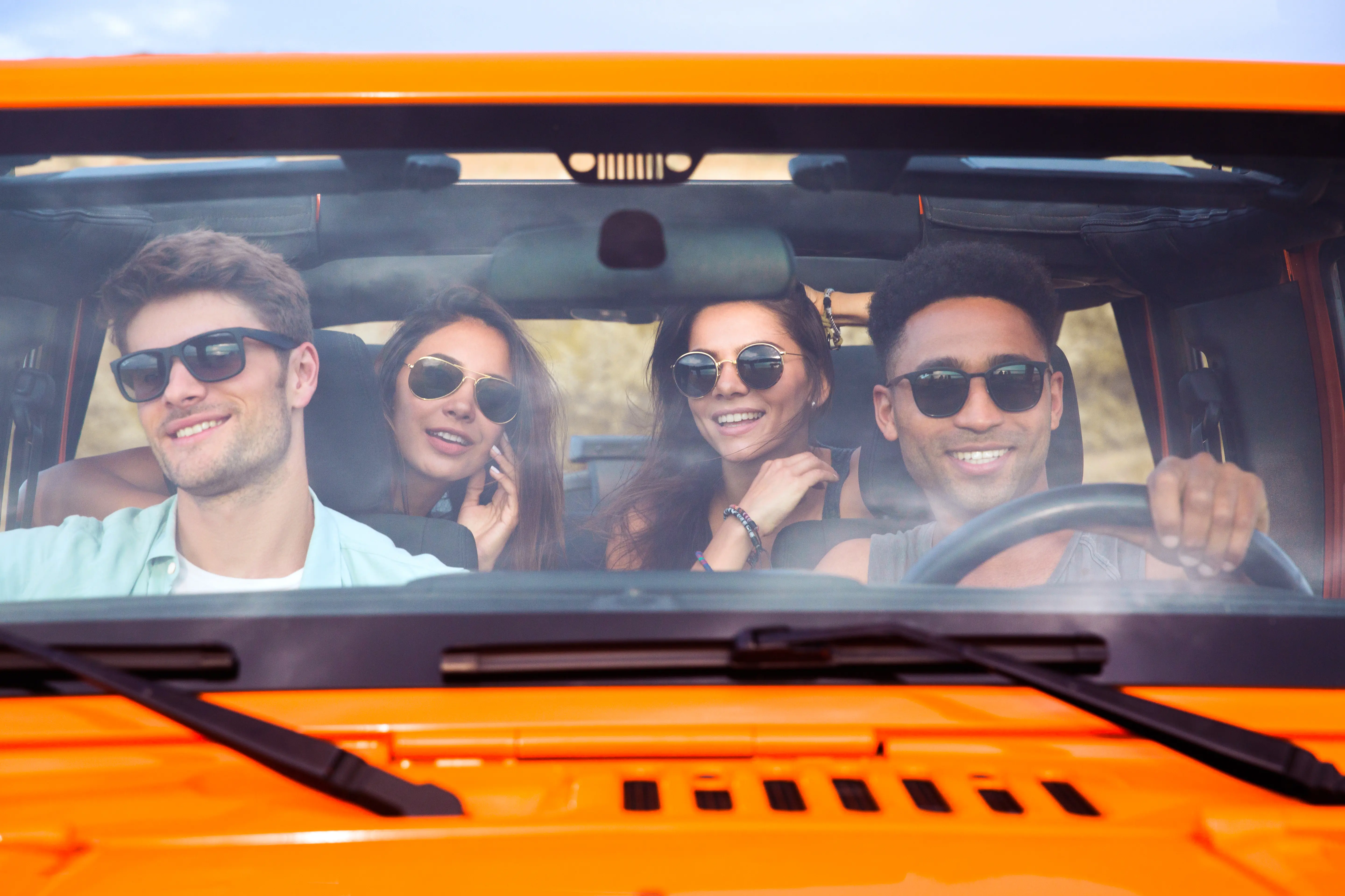 Four young friends sitting in an orange jeep preparing for a drive