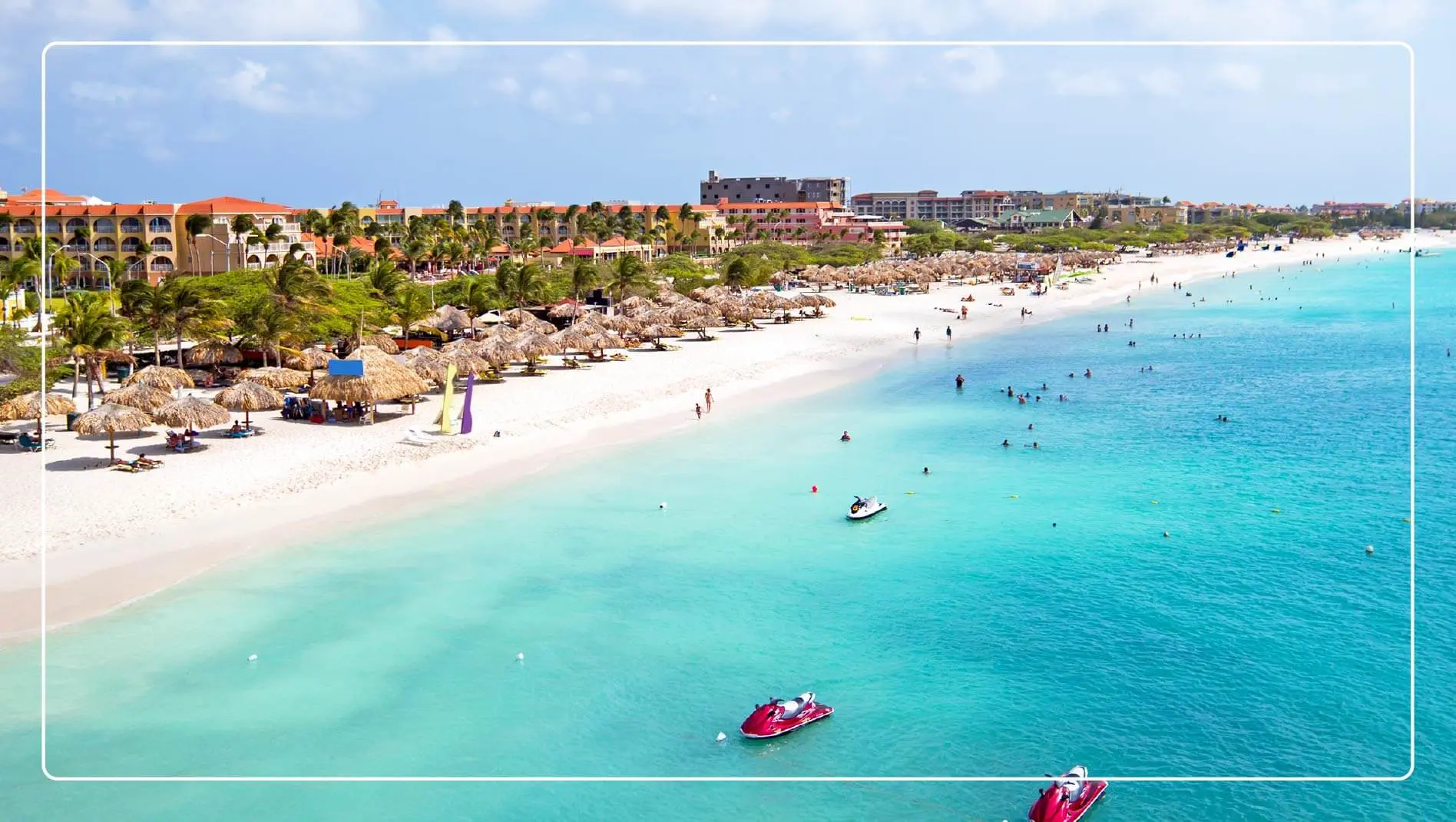 An aerial view of a beach in Aruba with jetskis in the foreground.
