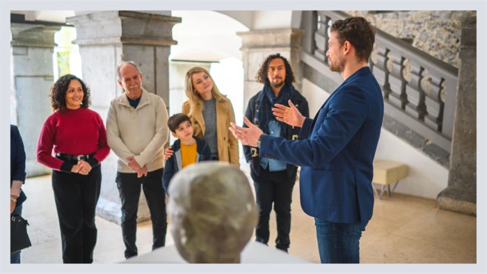 A group of people stand in a museum while receiving a guided tour. 