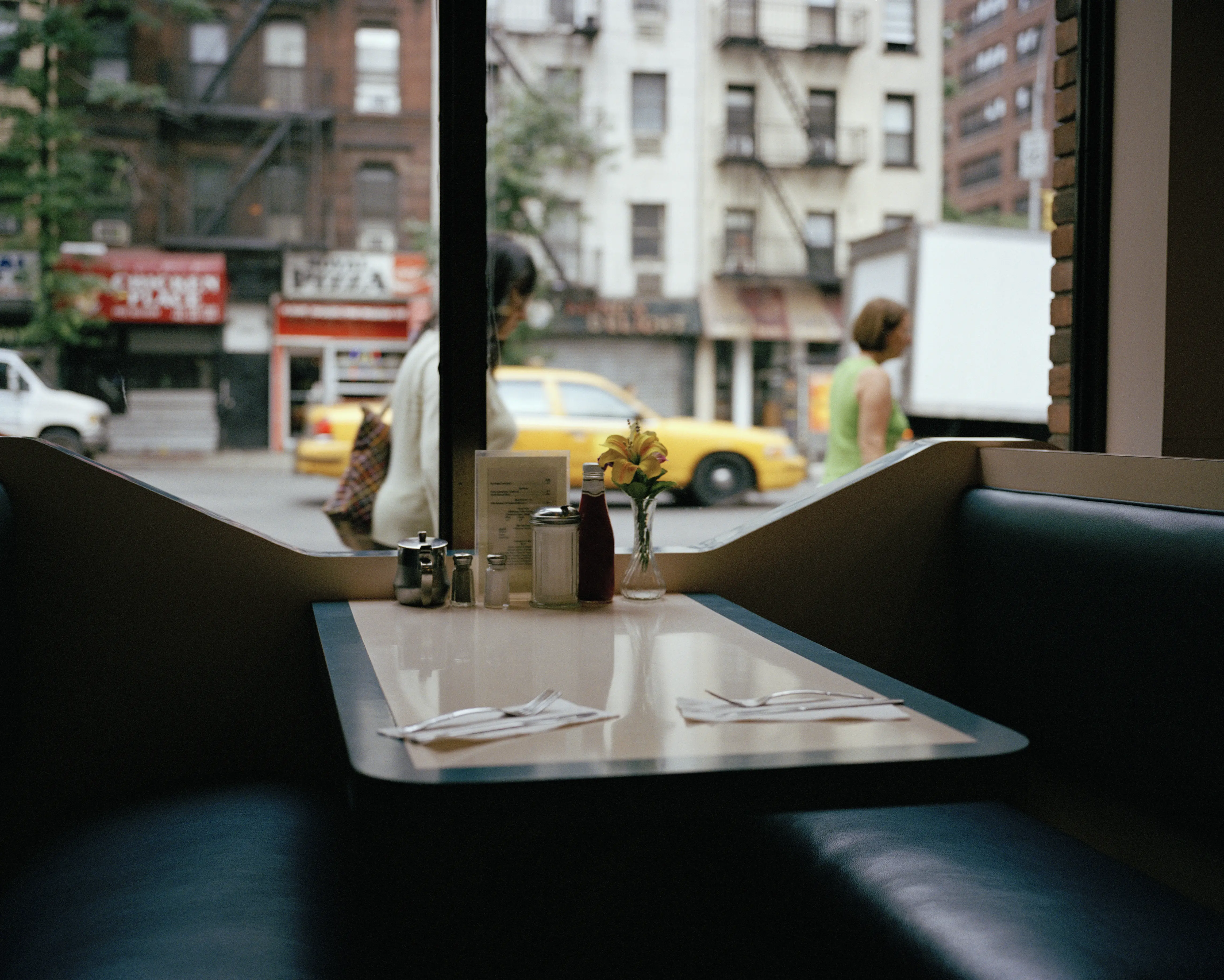 Interior image of an empty diner booth looking out the window onto a New York City street.