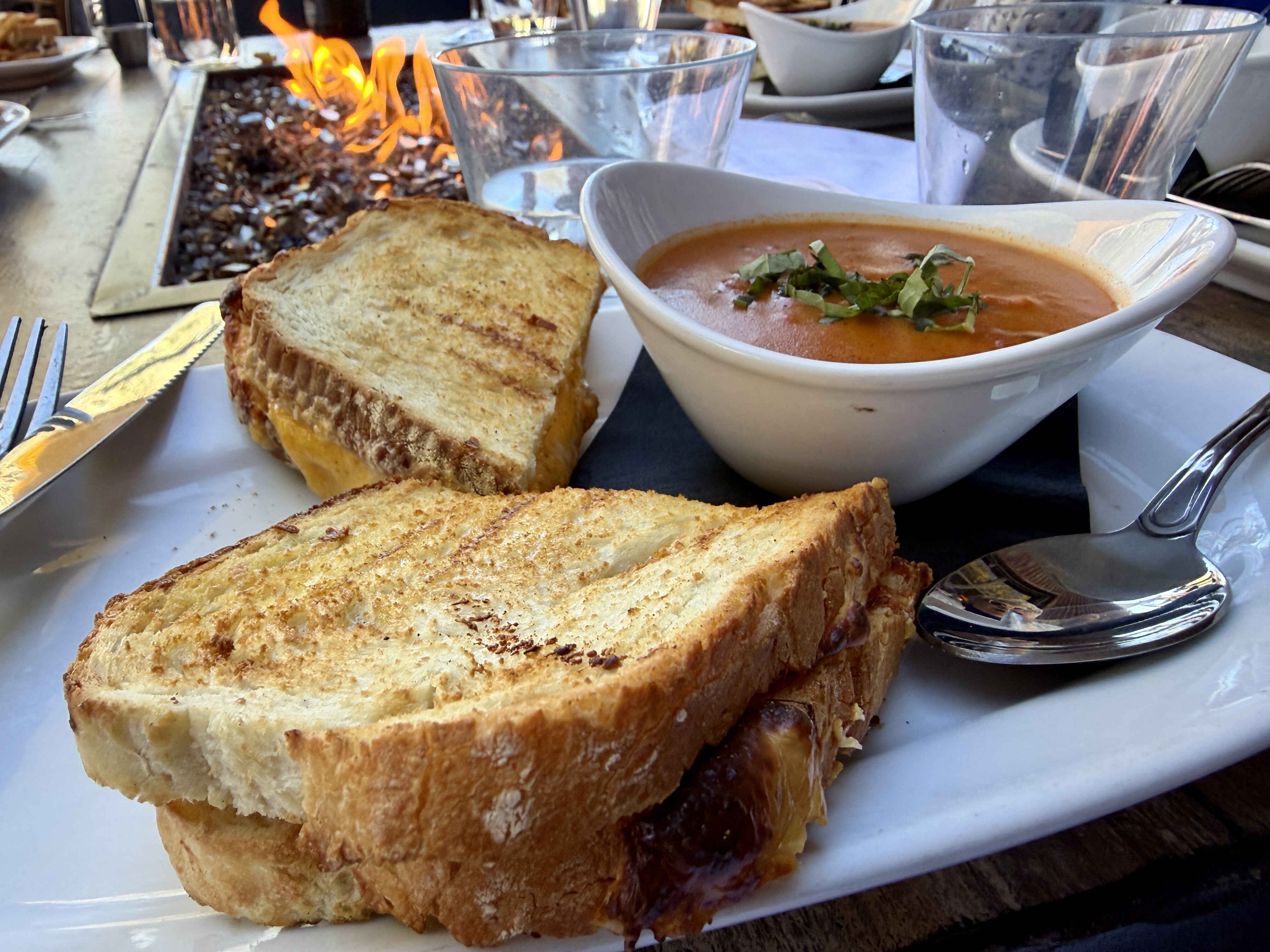 Toasted grilled cheese sandwich on a white plate accompanied by a bowl of tomato soup