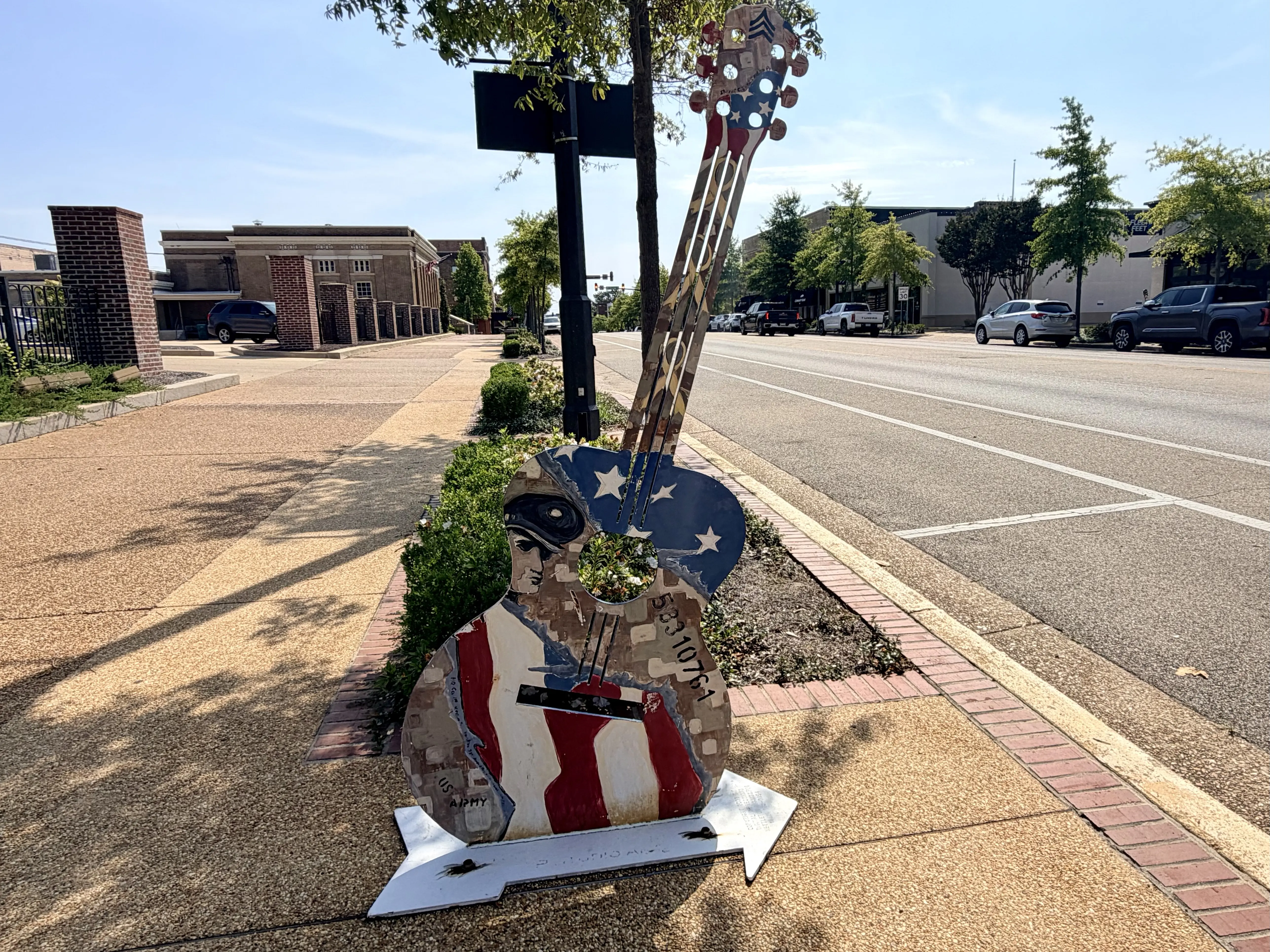 On the sidewalk in downtown Tupelo is a flat metal sculptue shaped like a guitar painted in an American flag motis and Elvis' face in his military dress uniform hat.